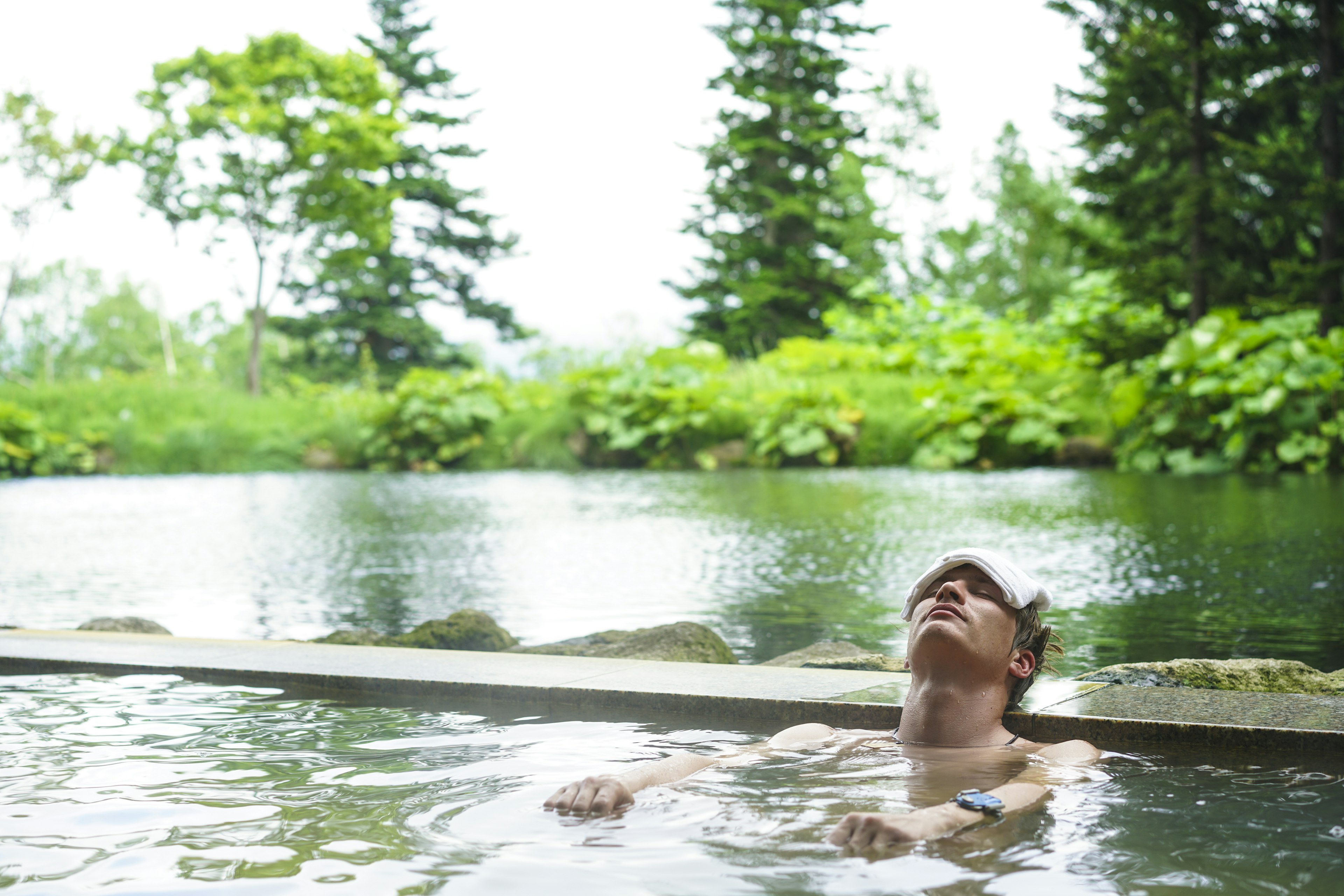 A man rests his head on the side of an onsen spring