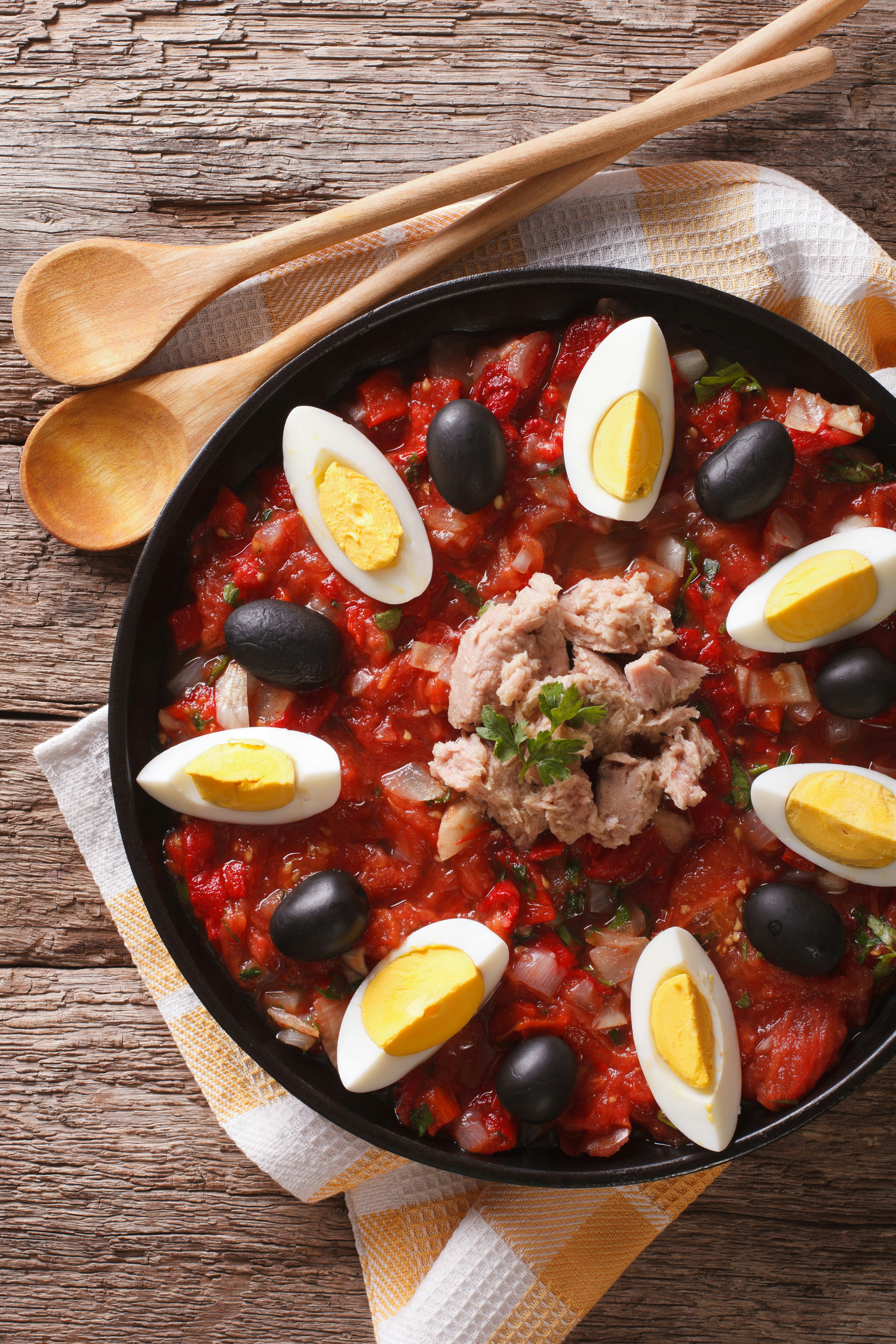 Mechouia salad (slata mechouia) with vegetables, tuna and eggs in a black bowl on a wooden table