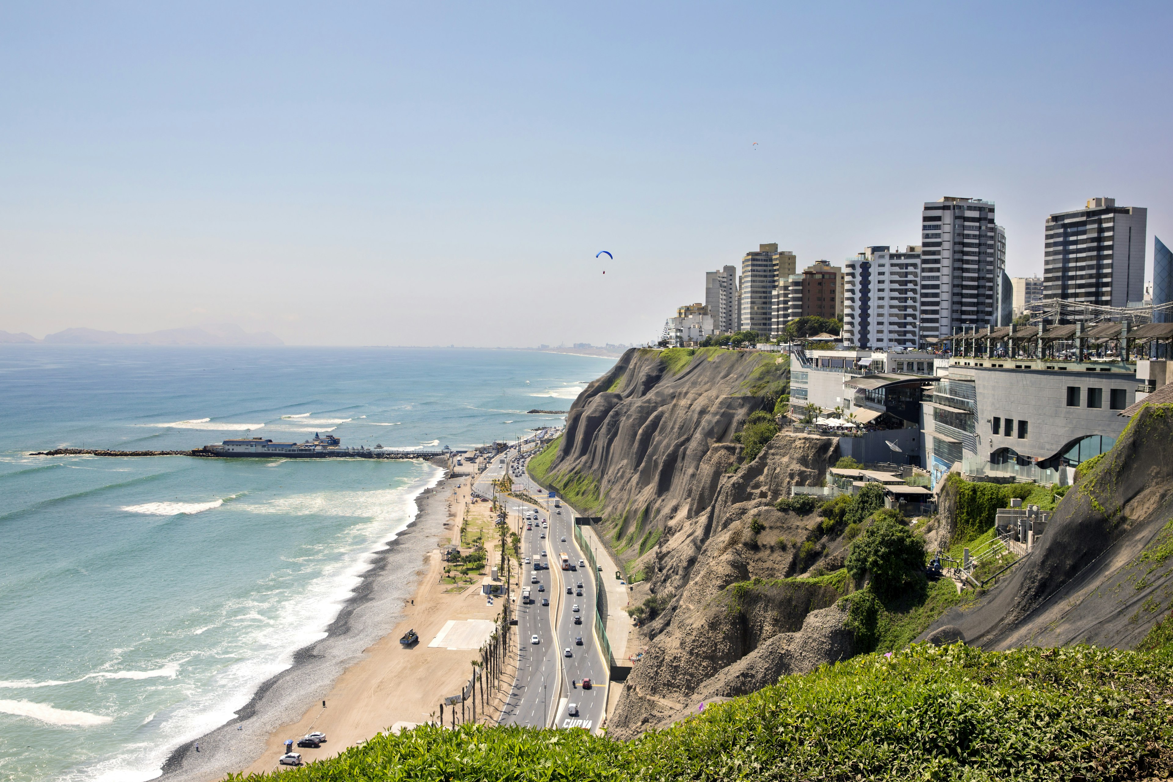 Aerial view of the coastline in Lima with a paraglider in the sky.