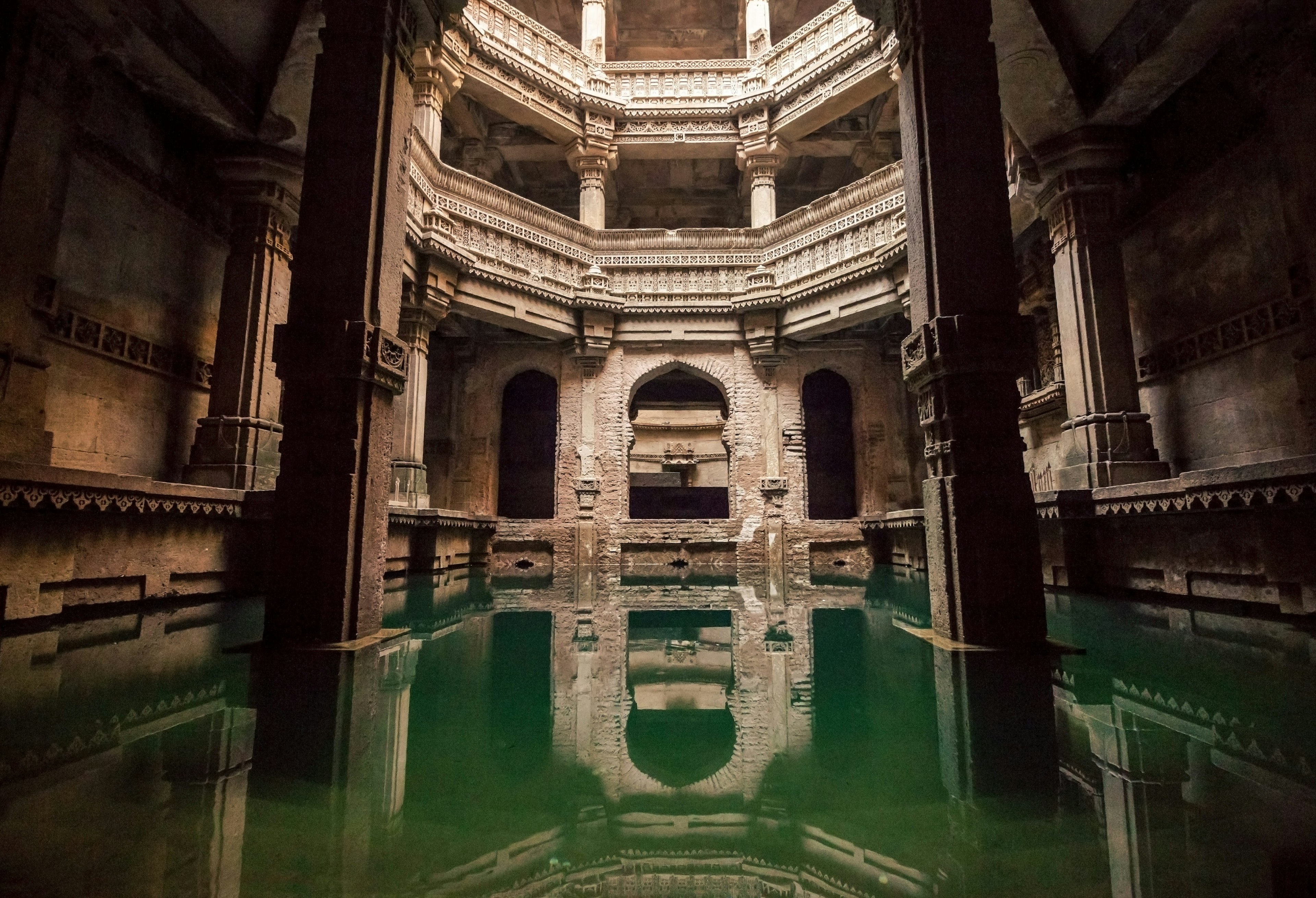 Inside the Adalaj Stepwell, with intricate carvings and green water pooled at the bottom.