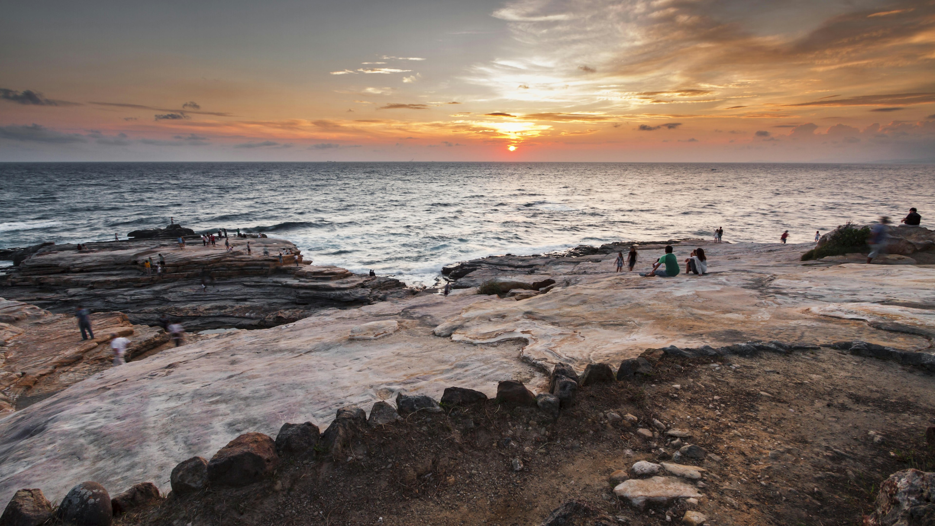 People gather to watch the sunset on the rocky coastline of Shirahama during summer.