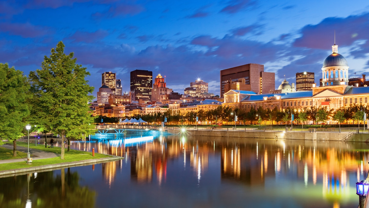 blue and purple clouds cross the sky at twilight as a beautiful skyline of lighted historic buildings is reflected in the waterfront of the Old Port of Montreal