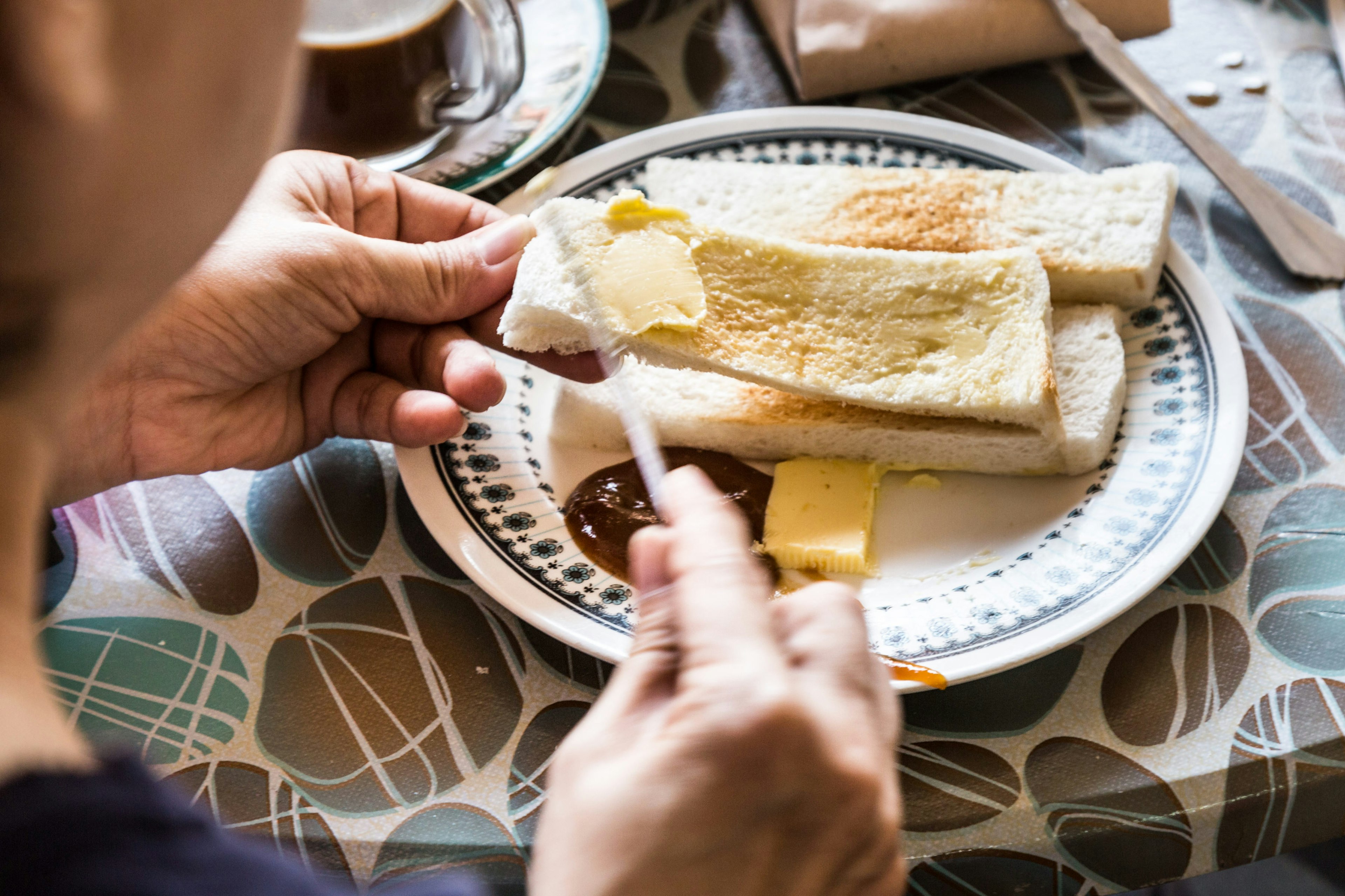 A man applying butter and kaya to steamed bread for a Malaysian breakfast.