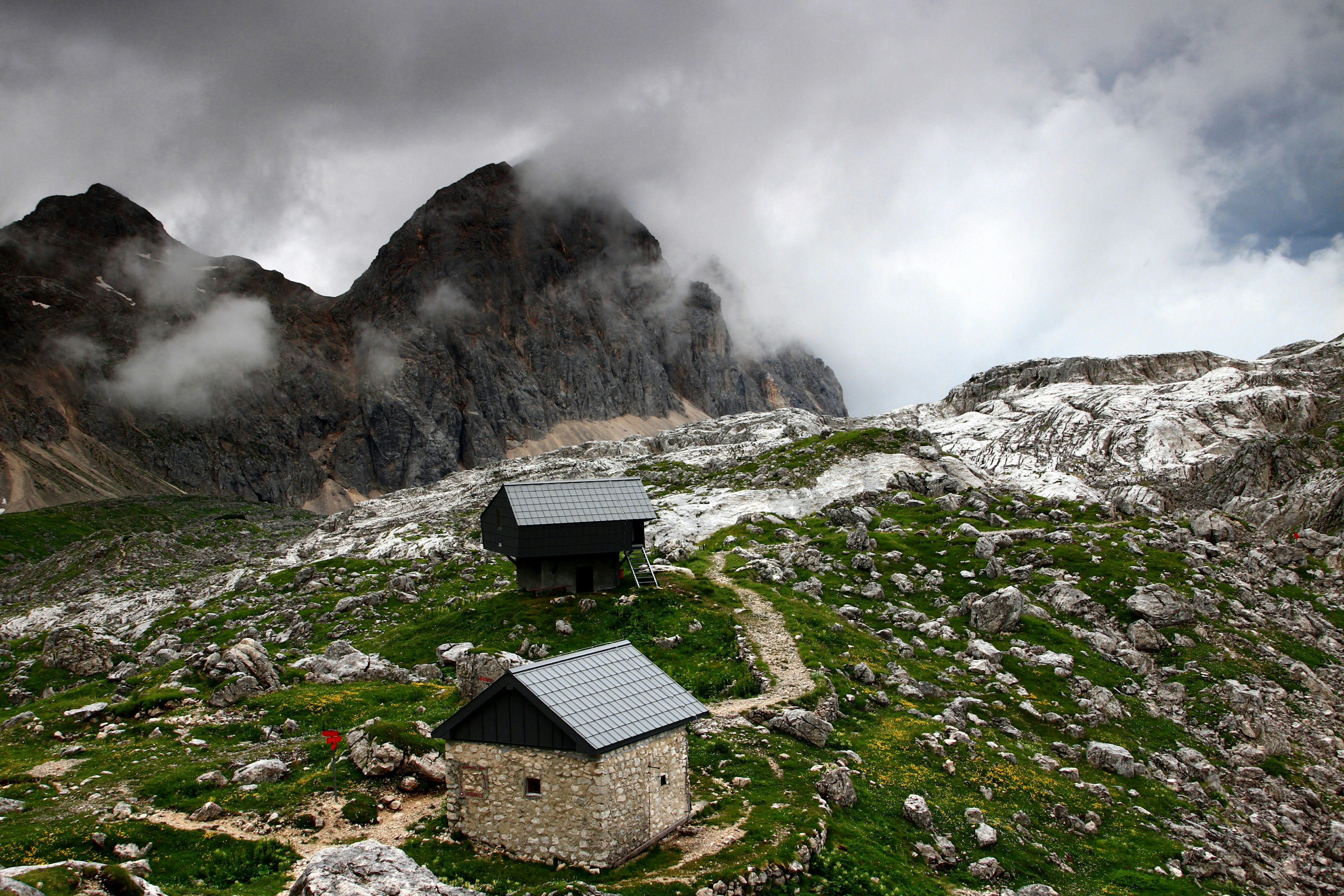 Rain clouds over Triglav Lakes Valley, Prehodavci pass, with winter room and shelter of a hut on the mountain.