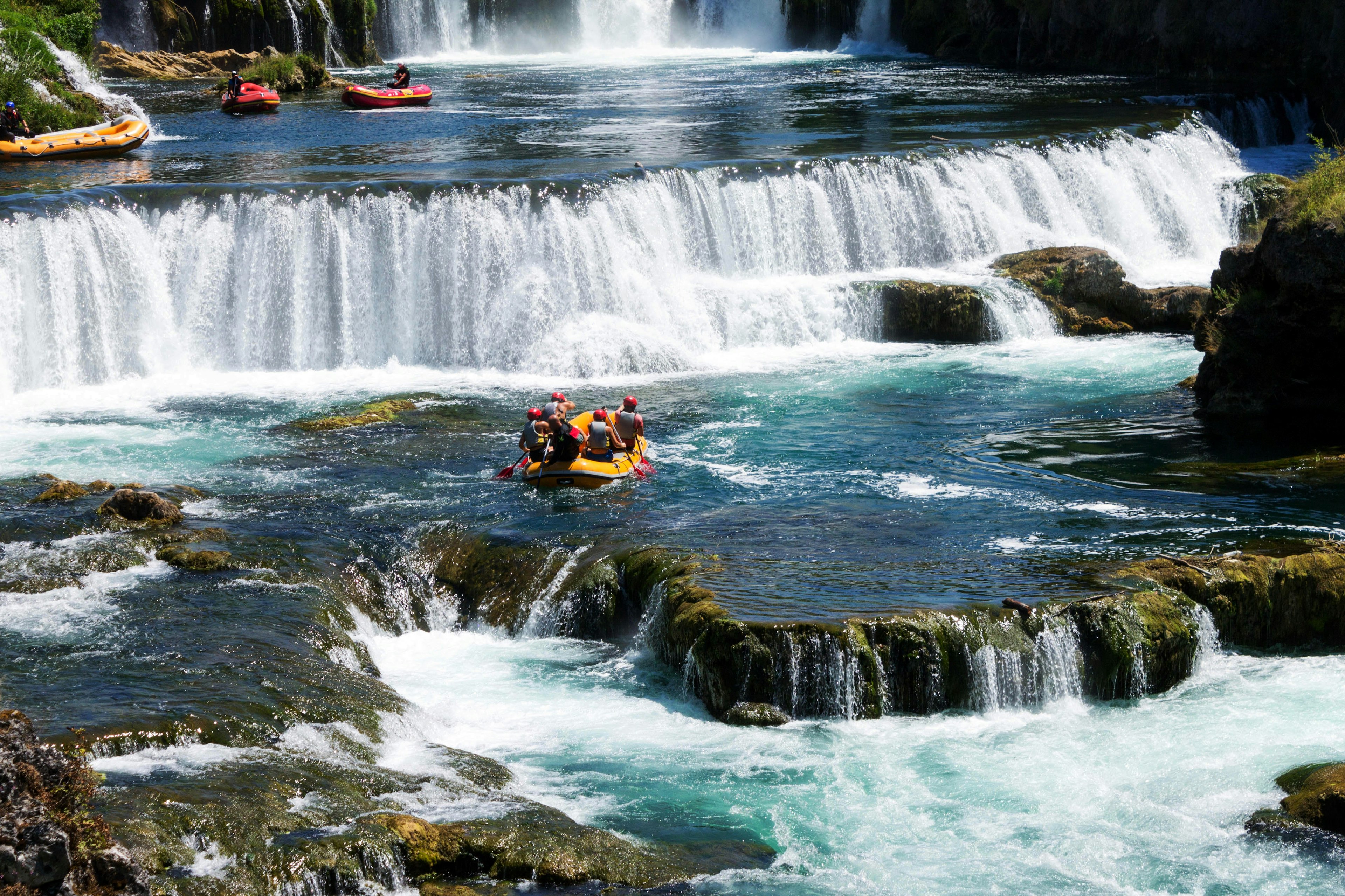 White water rafters paddle near waterfalls on a river in Bosnia and Herzegovina.