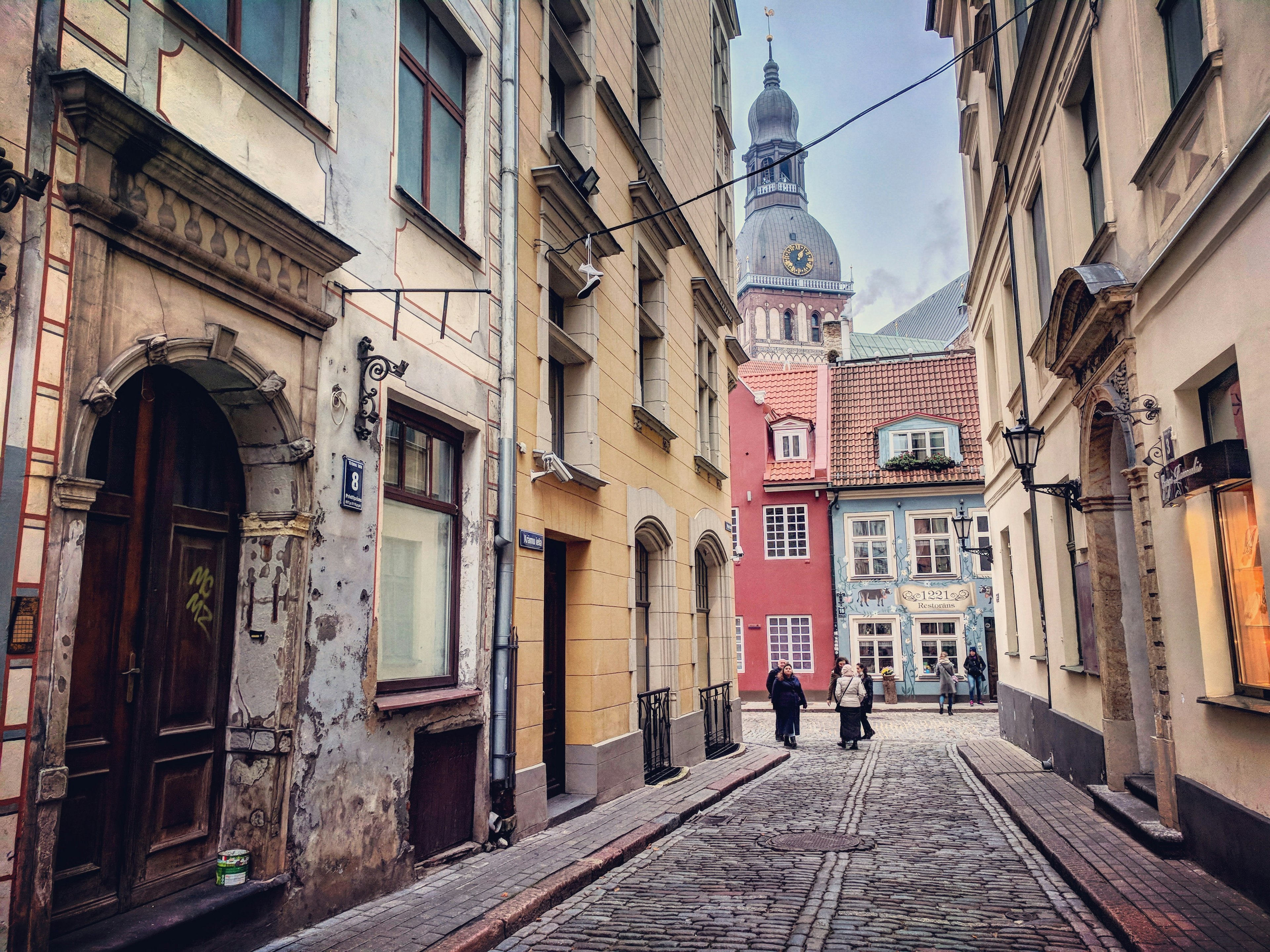 A cobbled street opening out onto a larger square with buildings in red and blue, and a church spire rising above