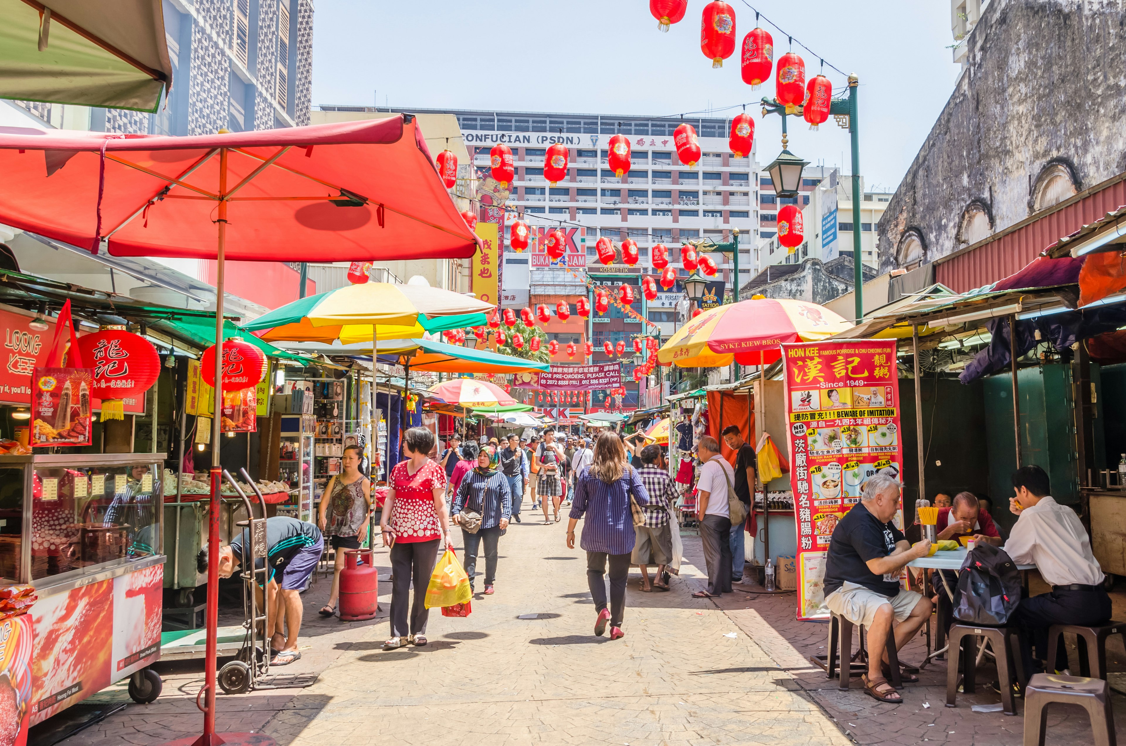 Shoppers and tourists wander down a street decorated with red paper lanterns and lined with food stalls