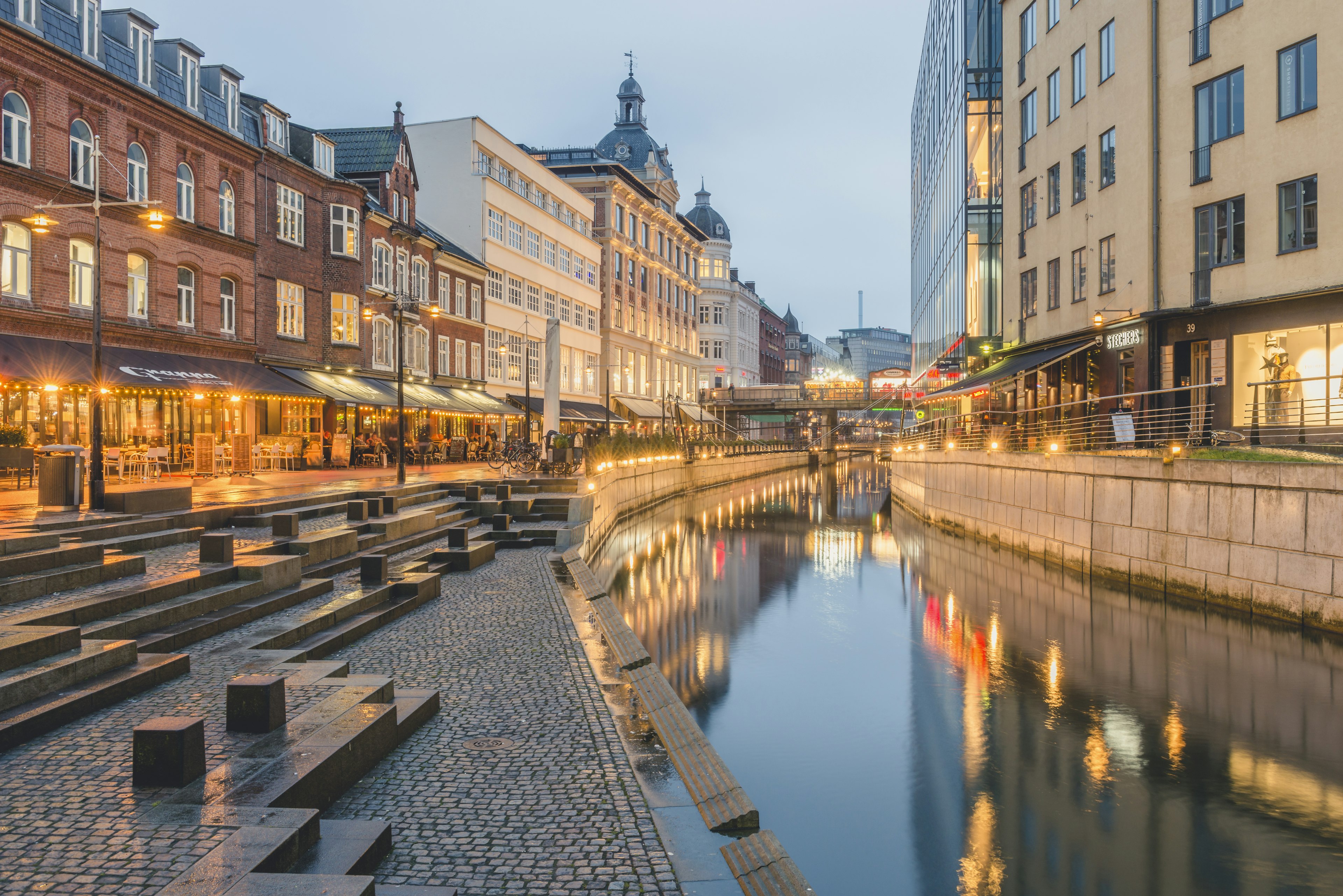 Buildings lit up at night along the Aarhus River.