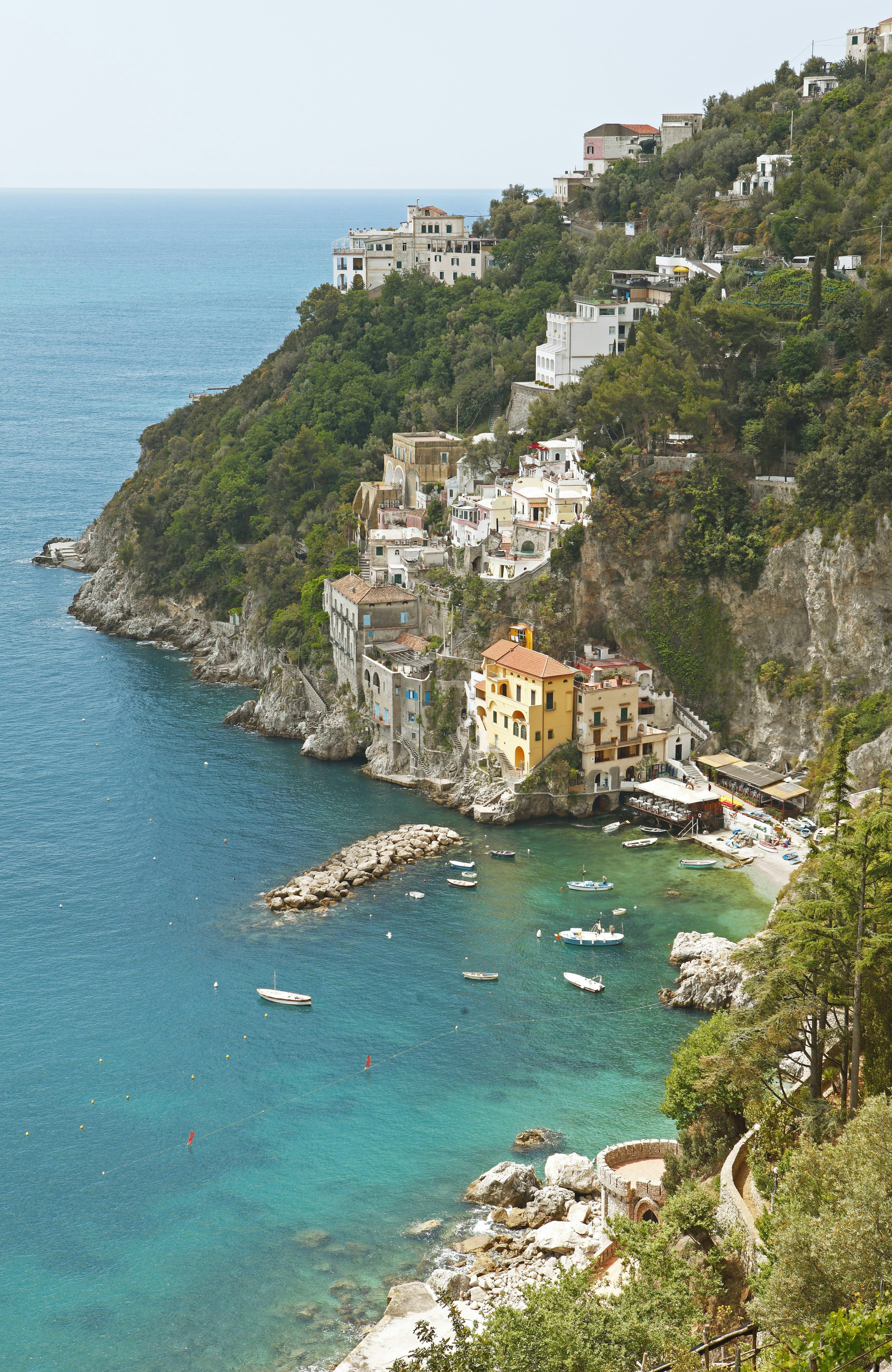 Small boats sit on the turquoise water and pastel-hued houses line the cliffs in Conca dei Marini