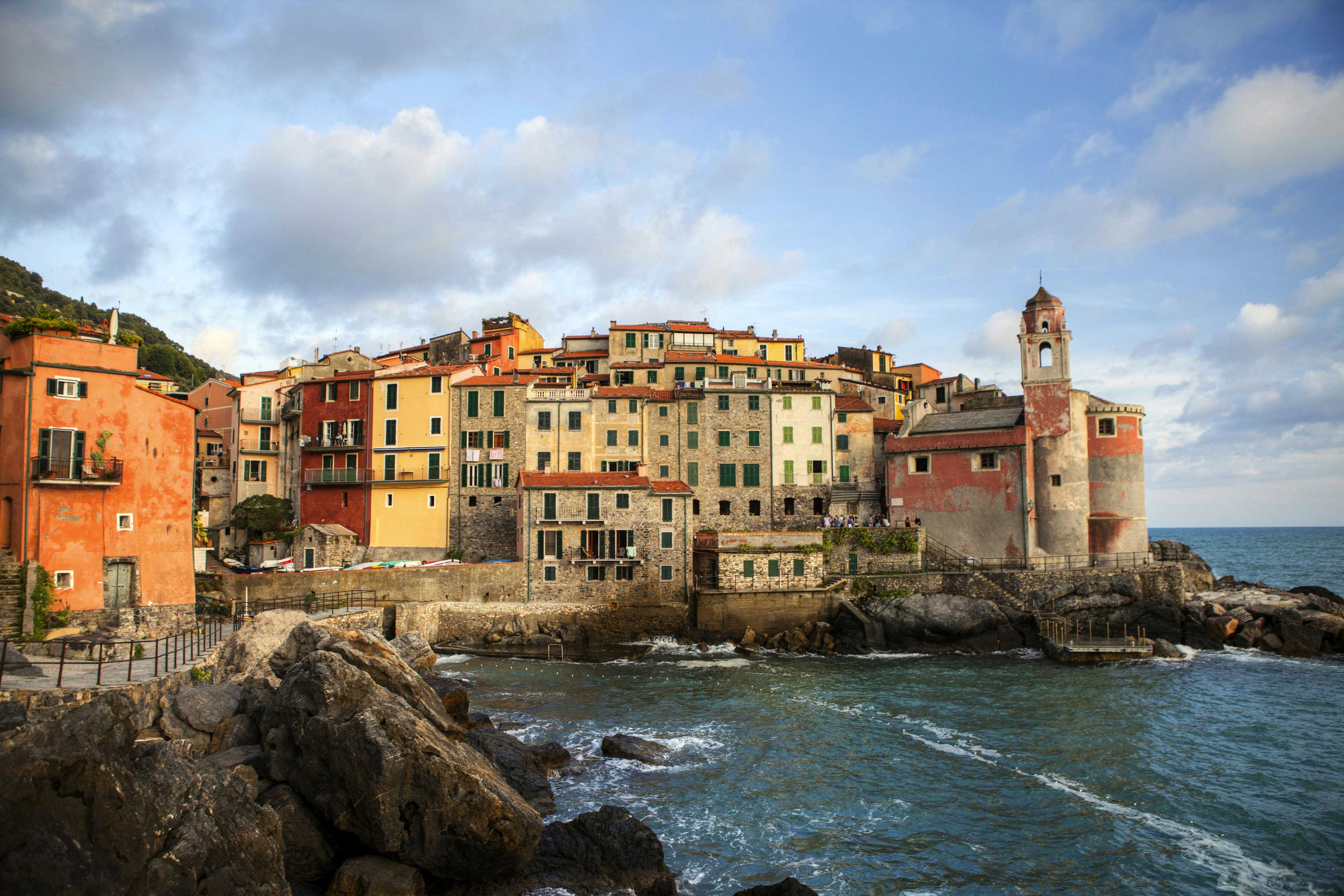 Tellaro's small harbour on a slightly overcast day. Narrow brick buildings are crammed in, side by side on a rocky outcrop.