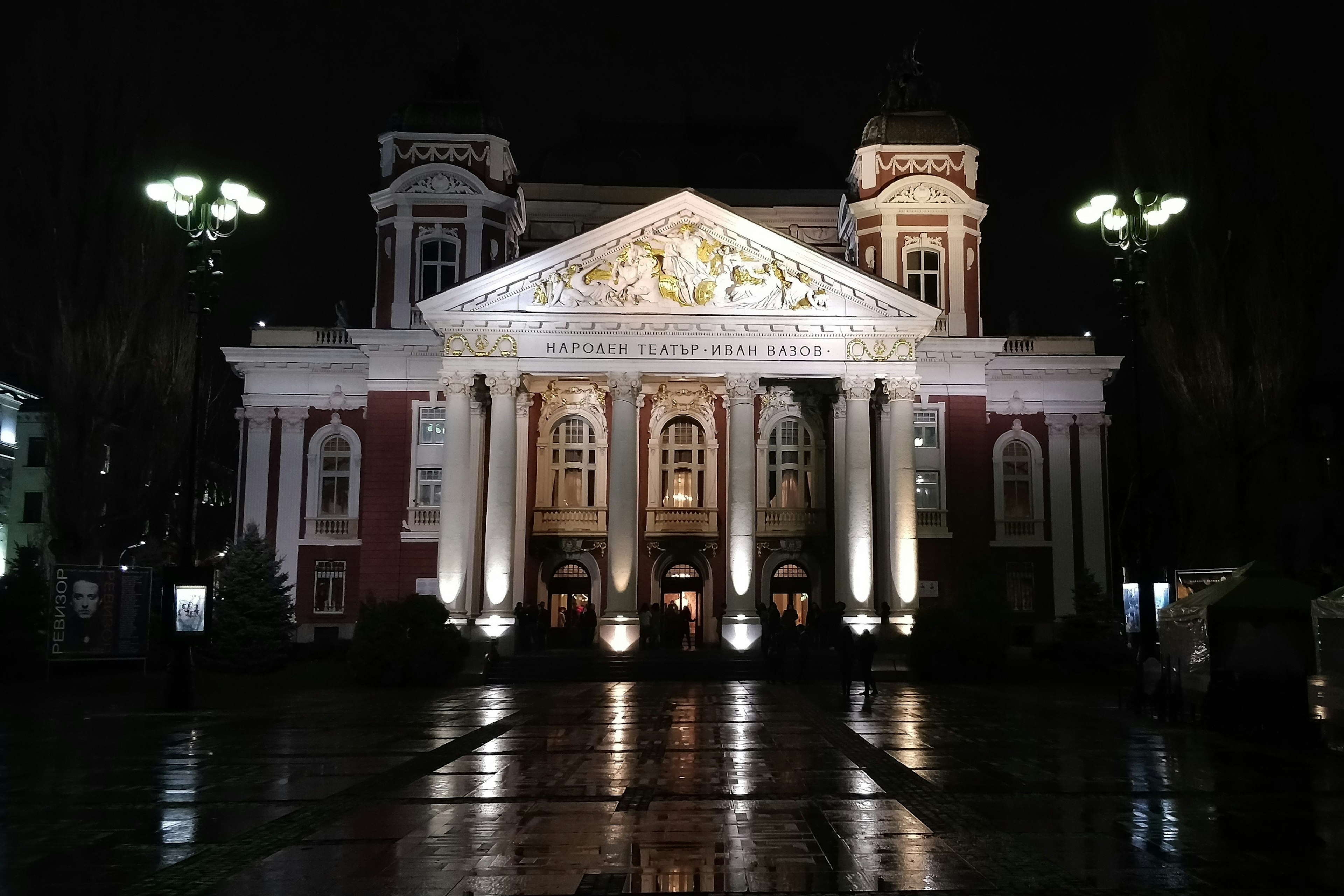 Exterior nighttime shot of a large red-coloured building, with a Greek-style columned exterior.