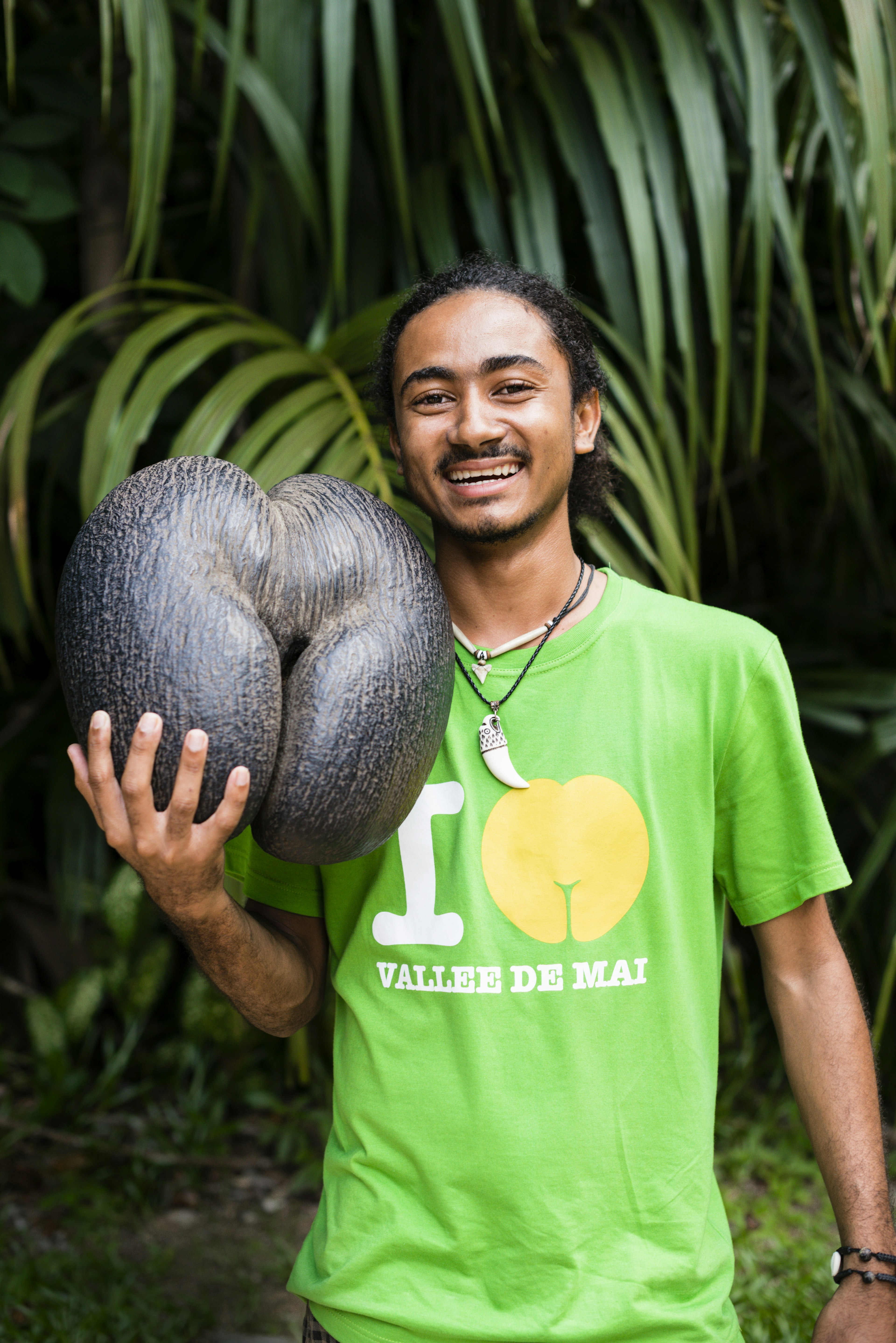 Local guide holding coco de mer seed, lush trees in the background.