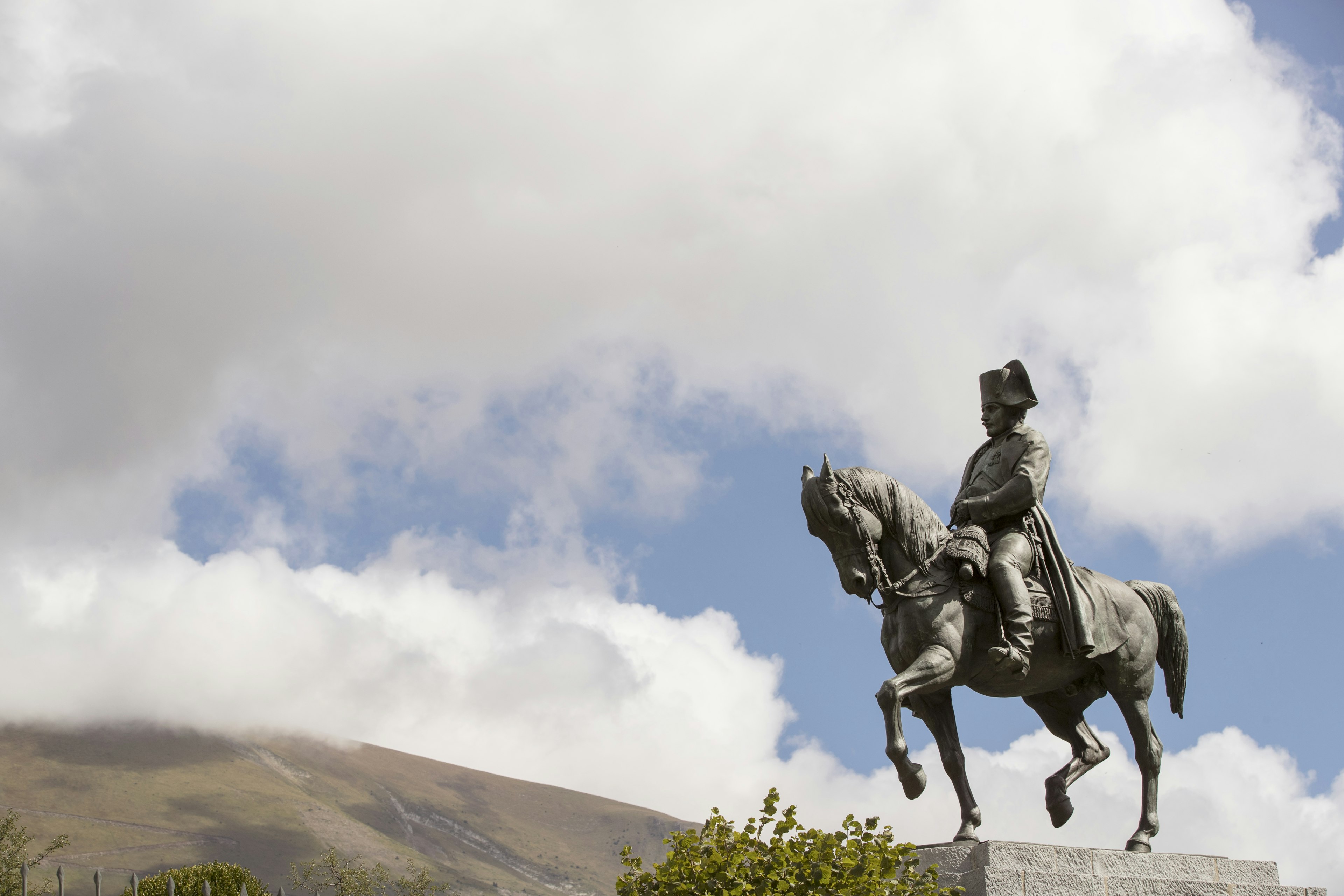 A horseback statue of Napoleon with his distinctive bicorn hat, with a cloudy sky in the background.