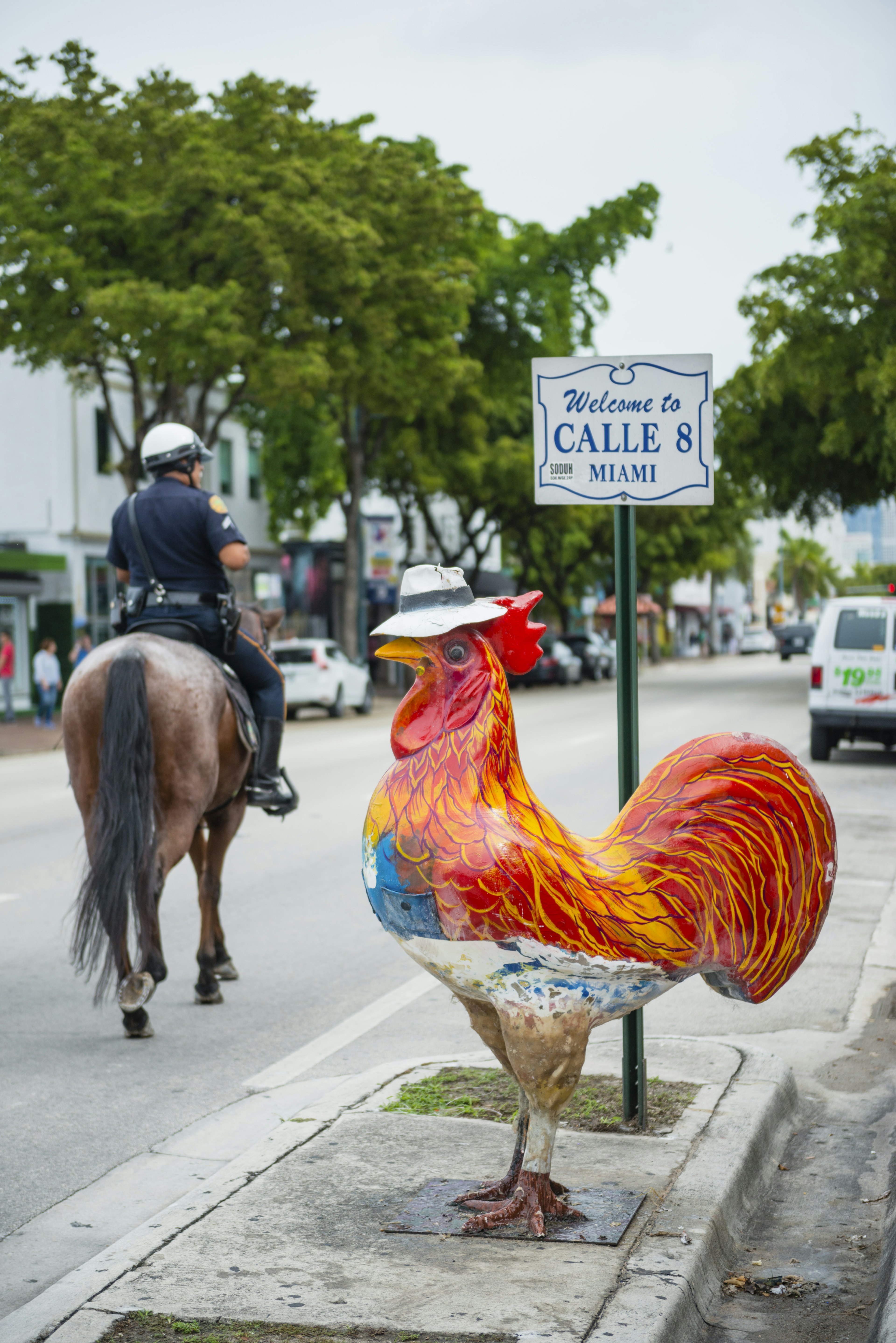 Welcome to Calle 8 sign, Little Havana, with rooster statue and mounted policeman.