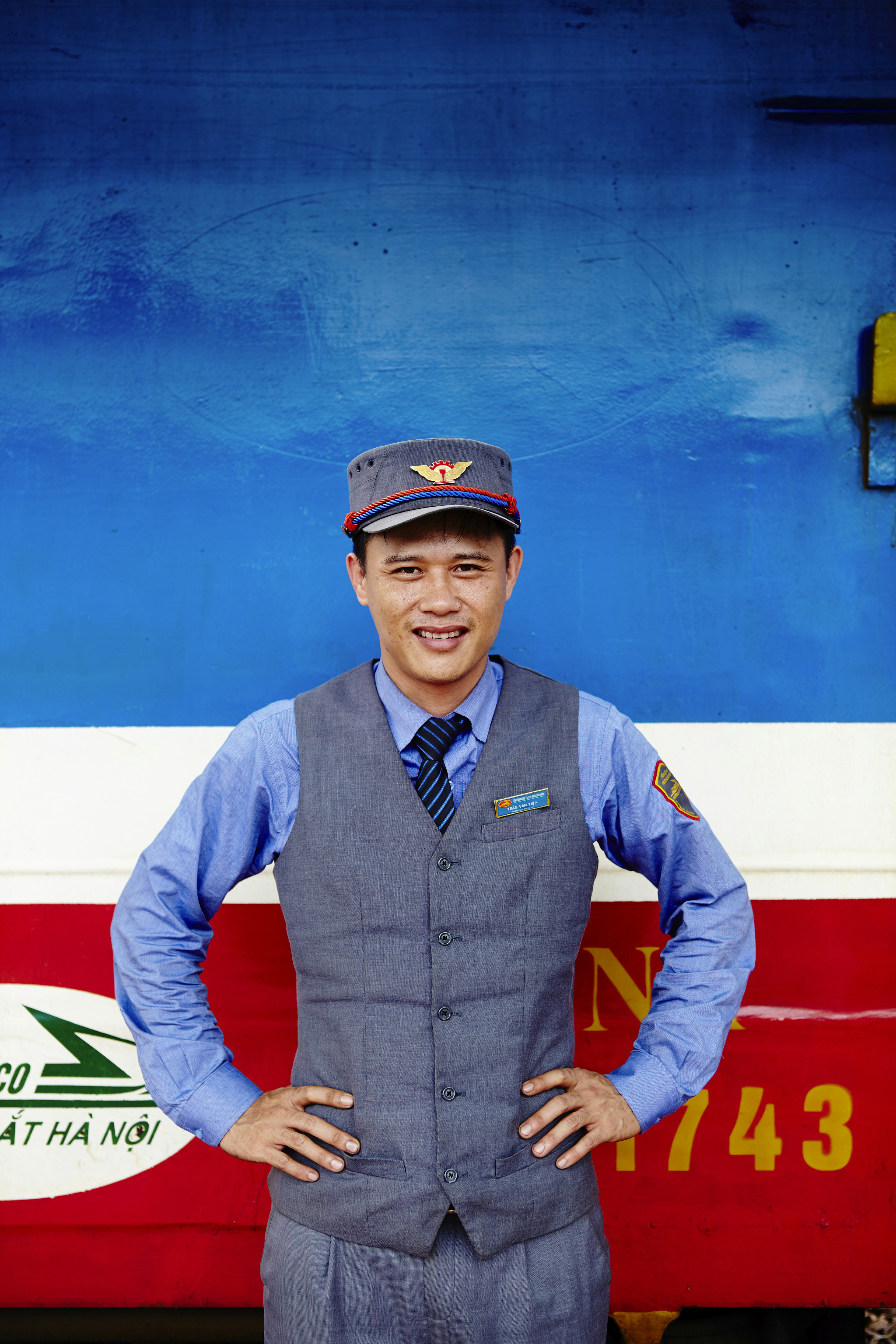 A railway guard standing in front of a red, white, and blue train.