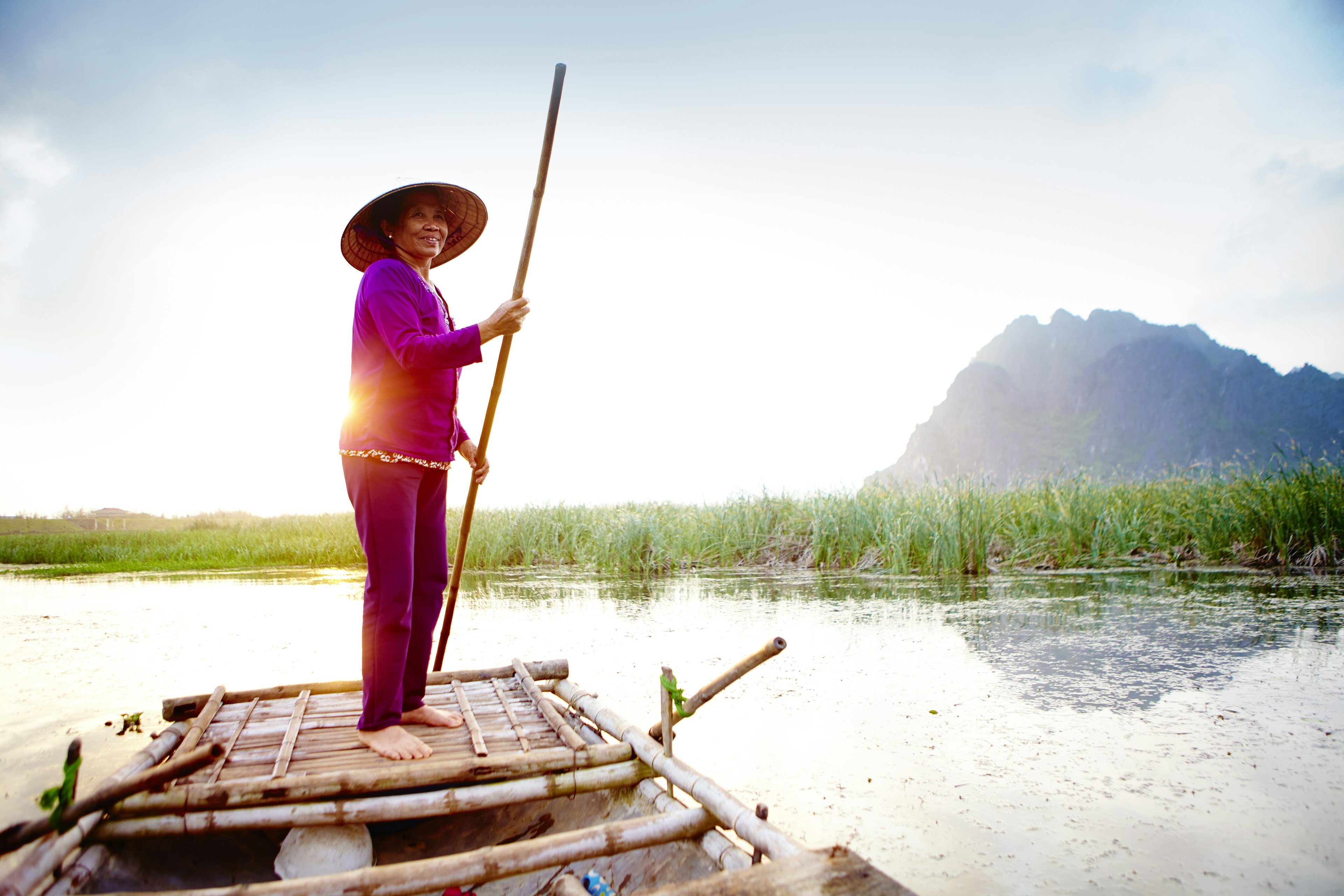 Woman with a pole on boat tour of Van Long Nature Reserve provides a relaxing way to enjoy the landscape.