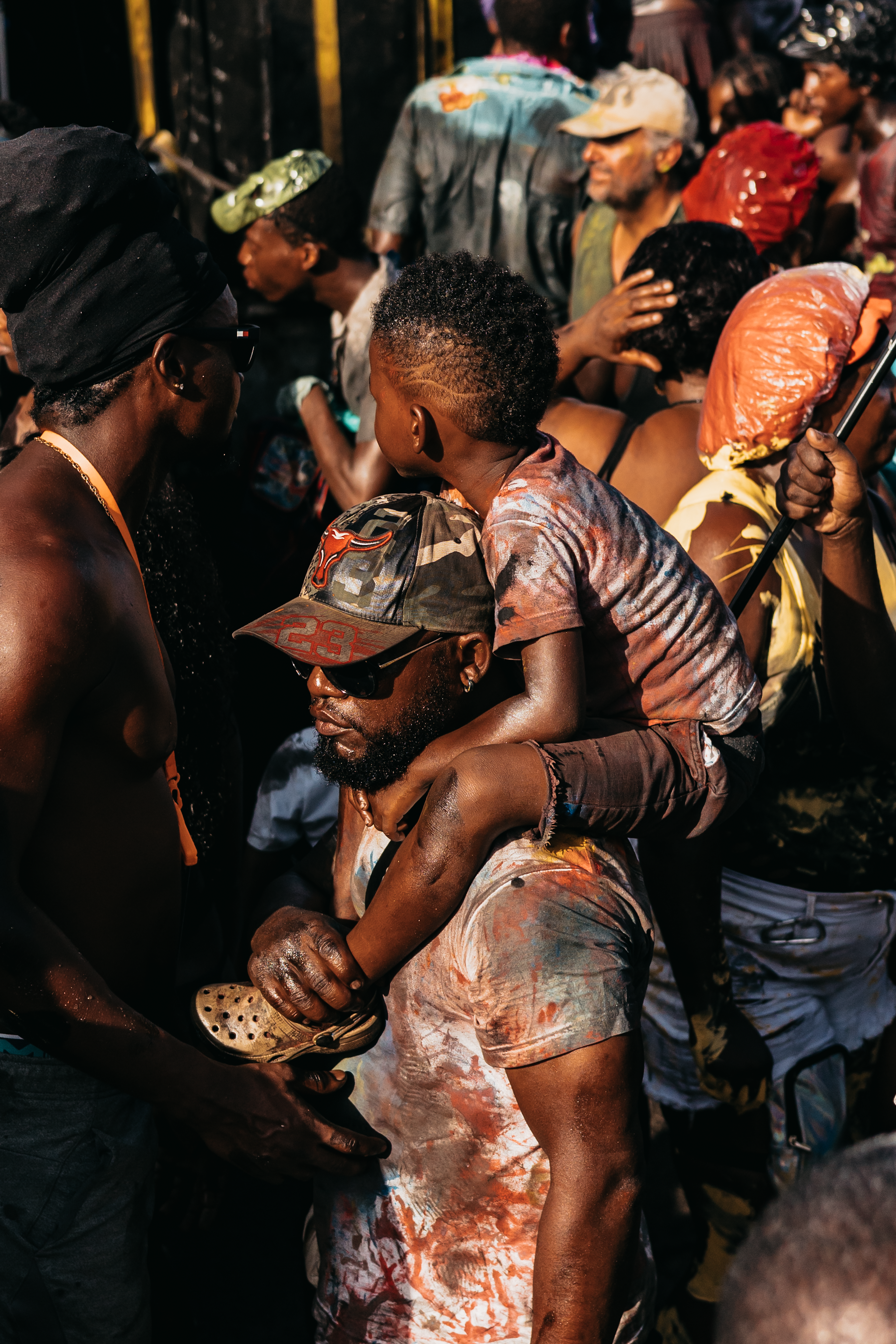 A young boy sits on the shoulders of an adult male during J'ouvert in Spicemas in Grenada. They're both covered in black oil and paint.