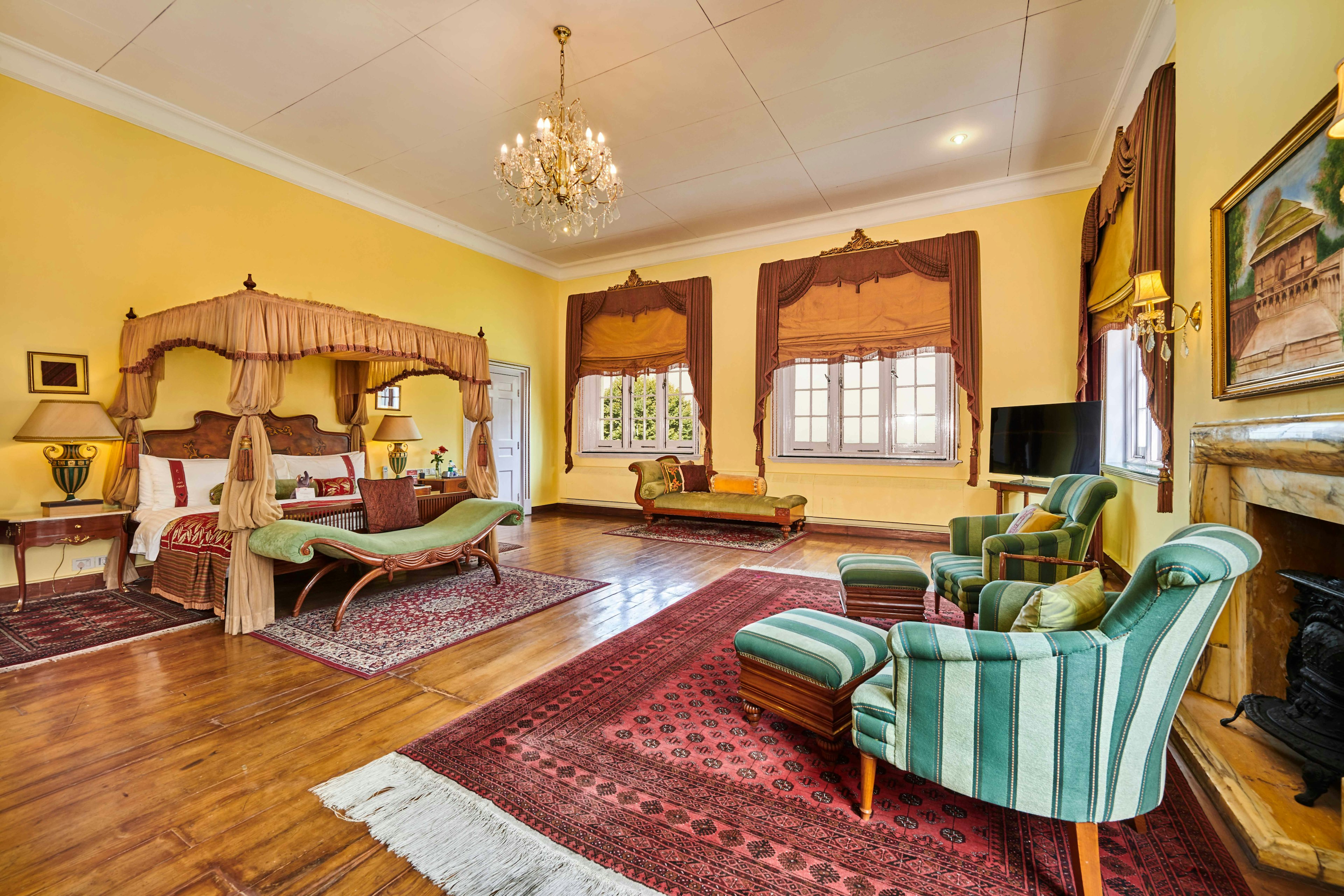 A grand bedroom with a four-poster bed, lounge area and two large windows