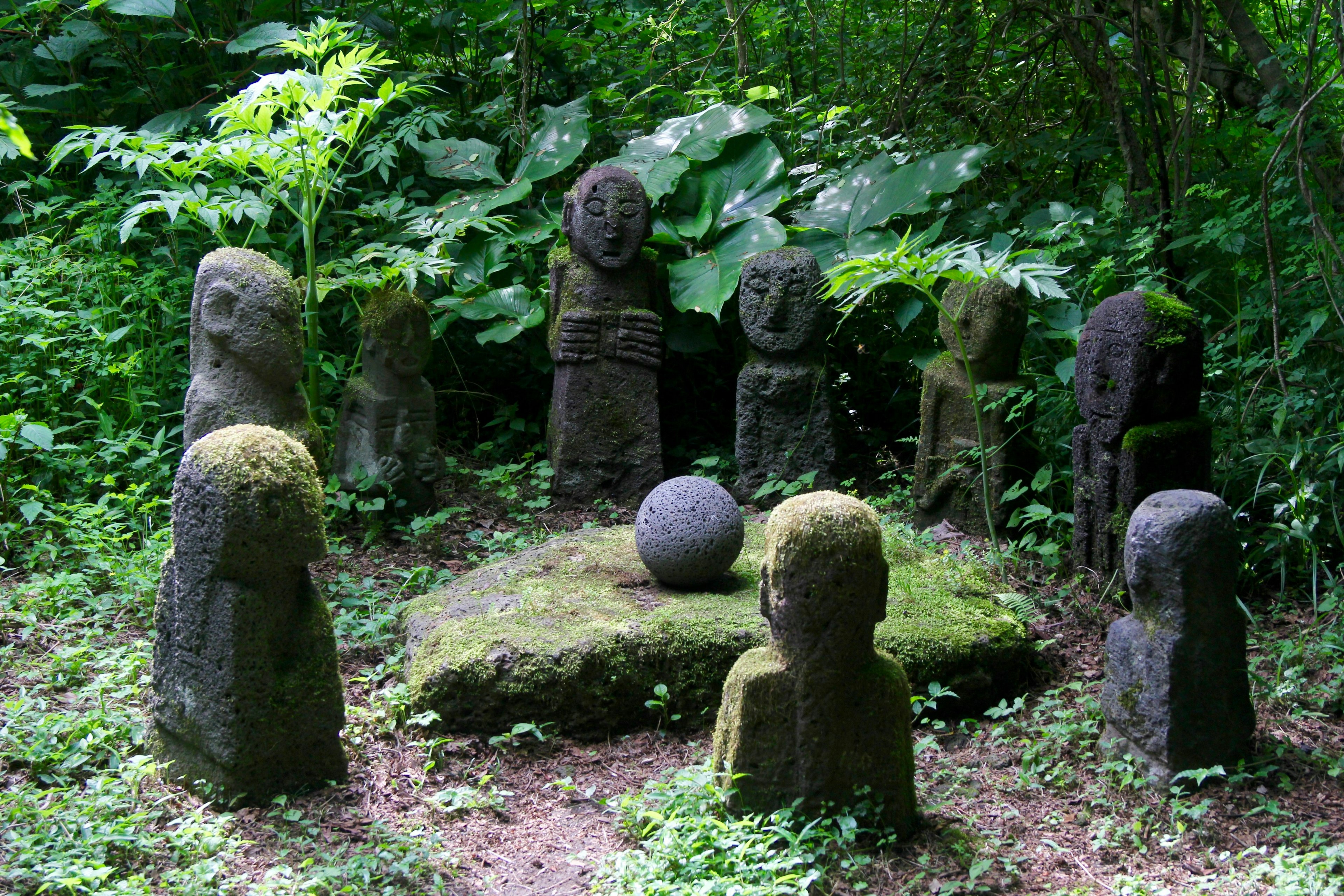 Statues of local spirits surrounding a stone ball in forest glade at Jeju Stone Park