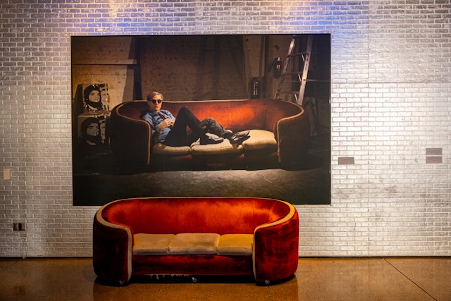 A red sofa in front of a painting of Andy Warhol reclining on the same sofa