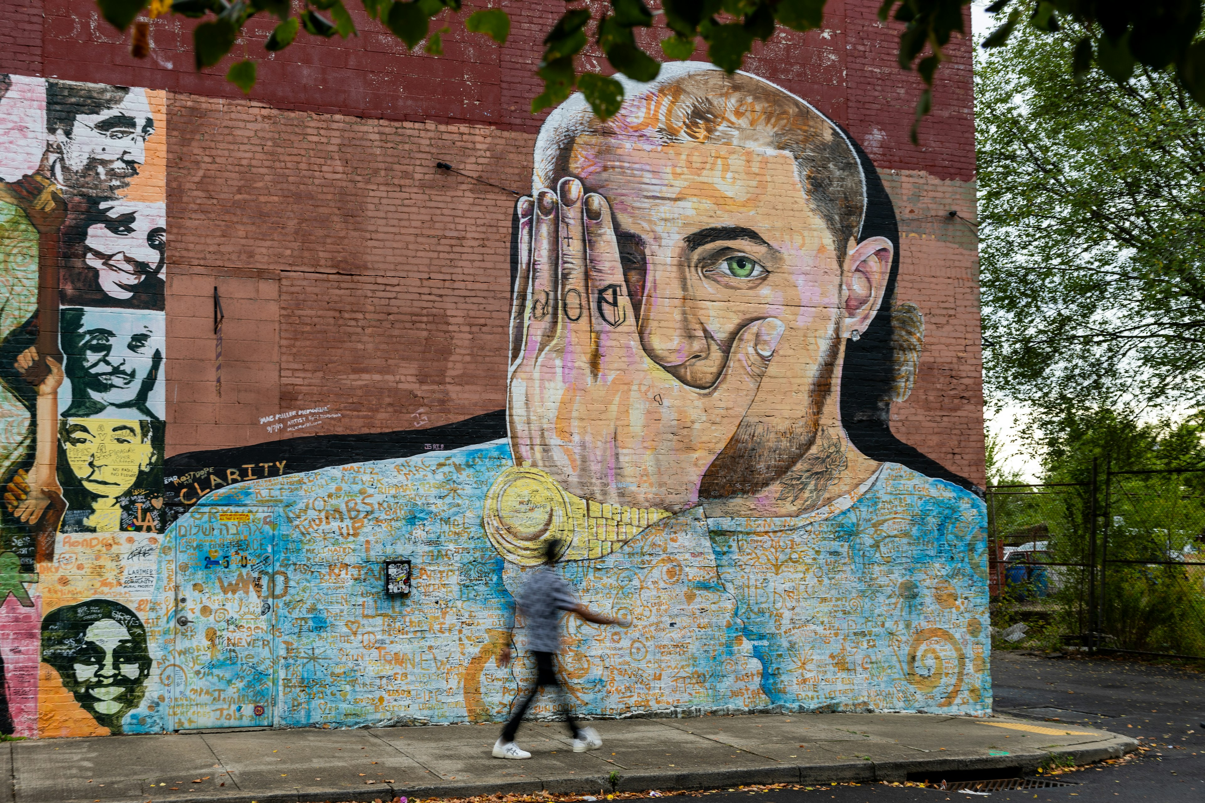 A man walks past a painted mural portrayinig a musical artist with his left hand over his right eye