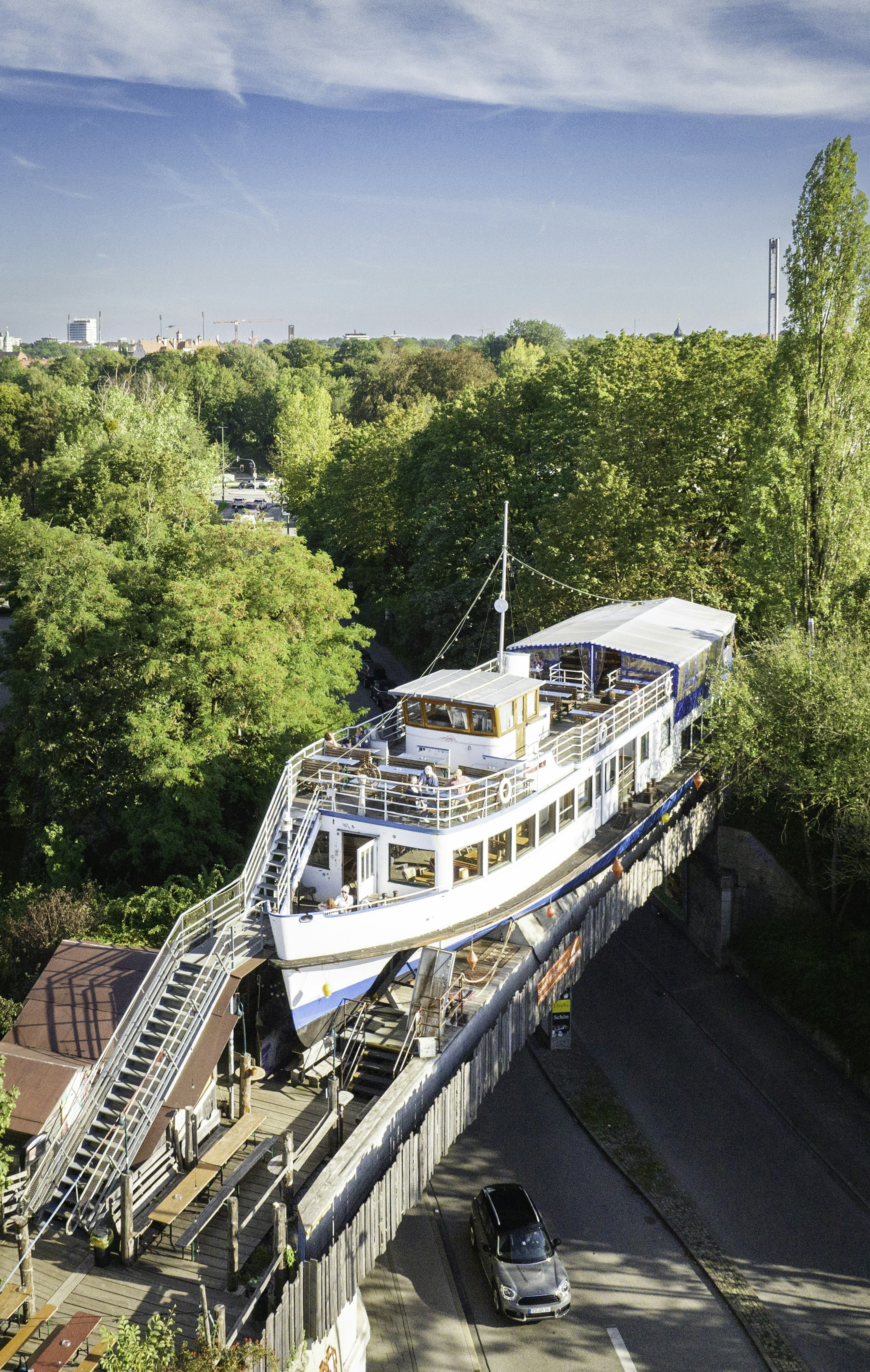 A passenger boat sits on a former railway bridge with a staircase leading up to its top deck. A car is seen passing under the bridge and boat.