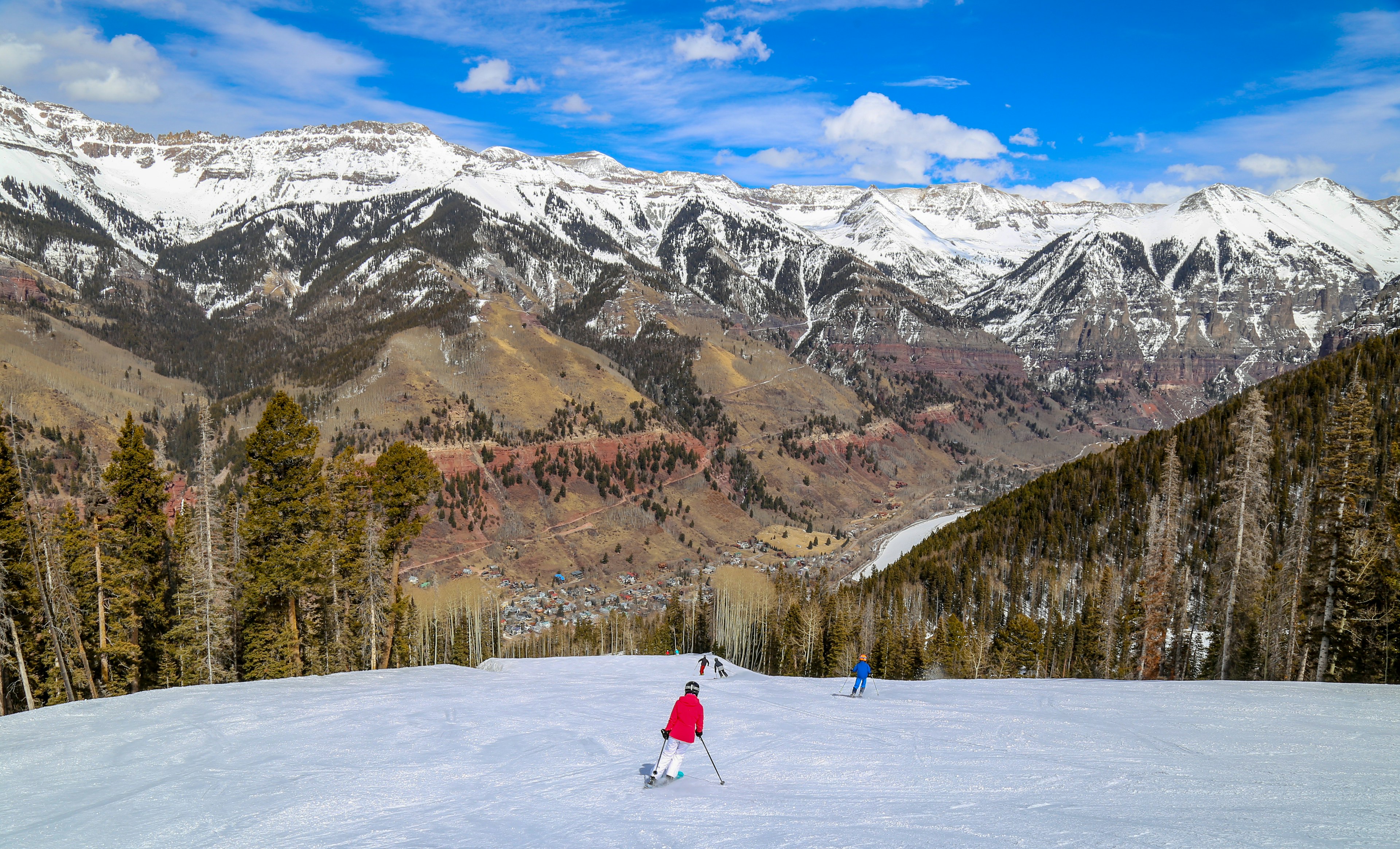 A skiier descends a slope with a view of the snow-covered Rockies in the distance, Telluride, Colorado, USA