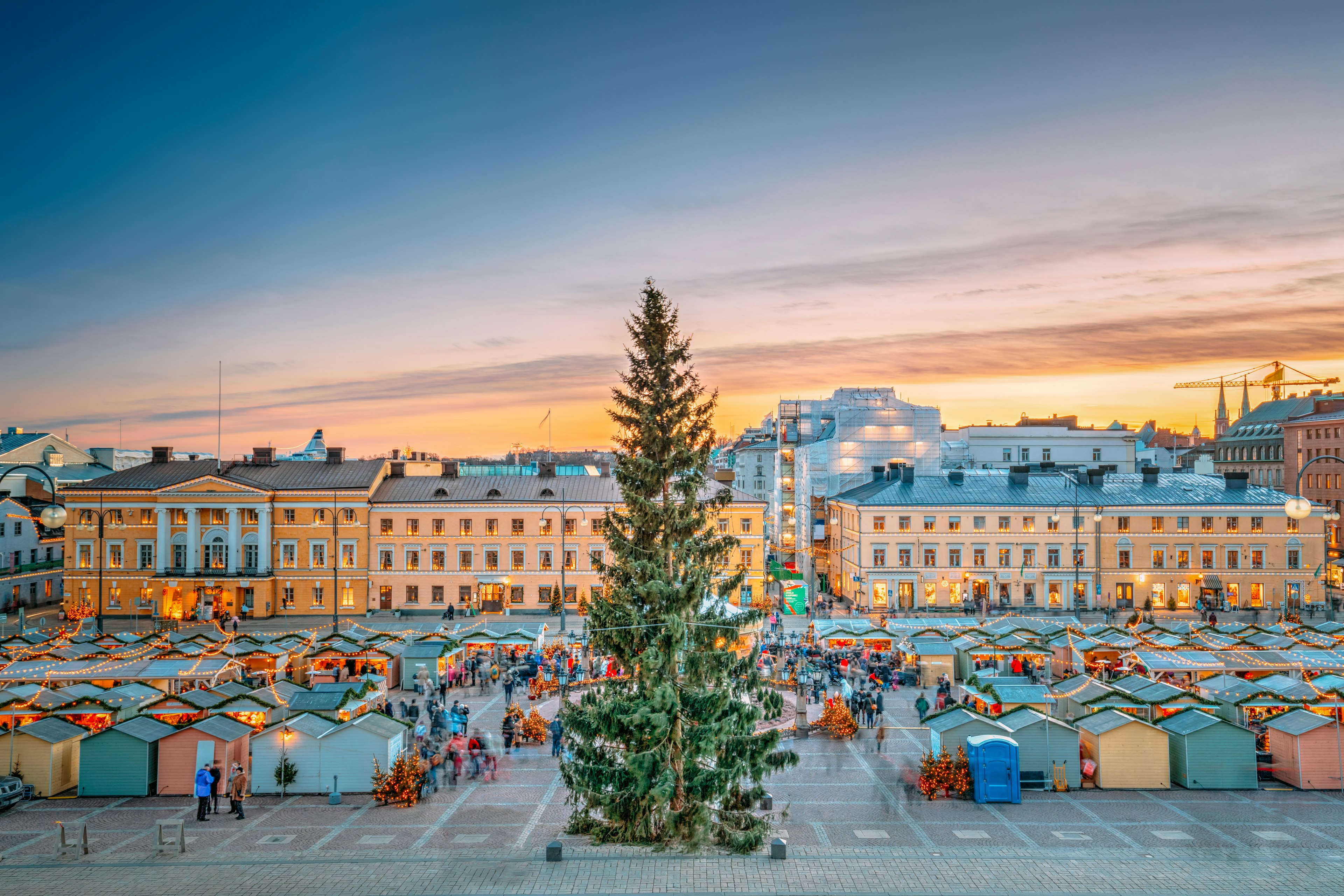 A large Christmas tree surrounded by pastel-colored wooden huts at a Christmas market