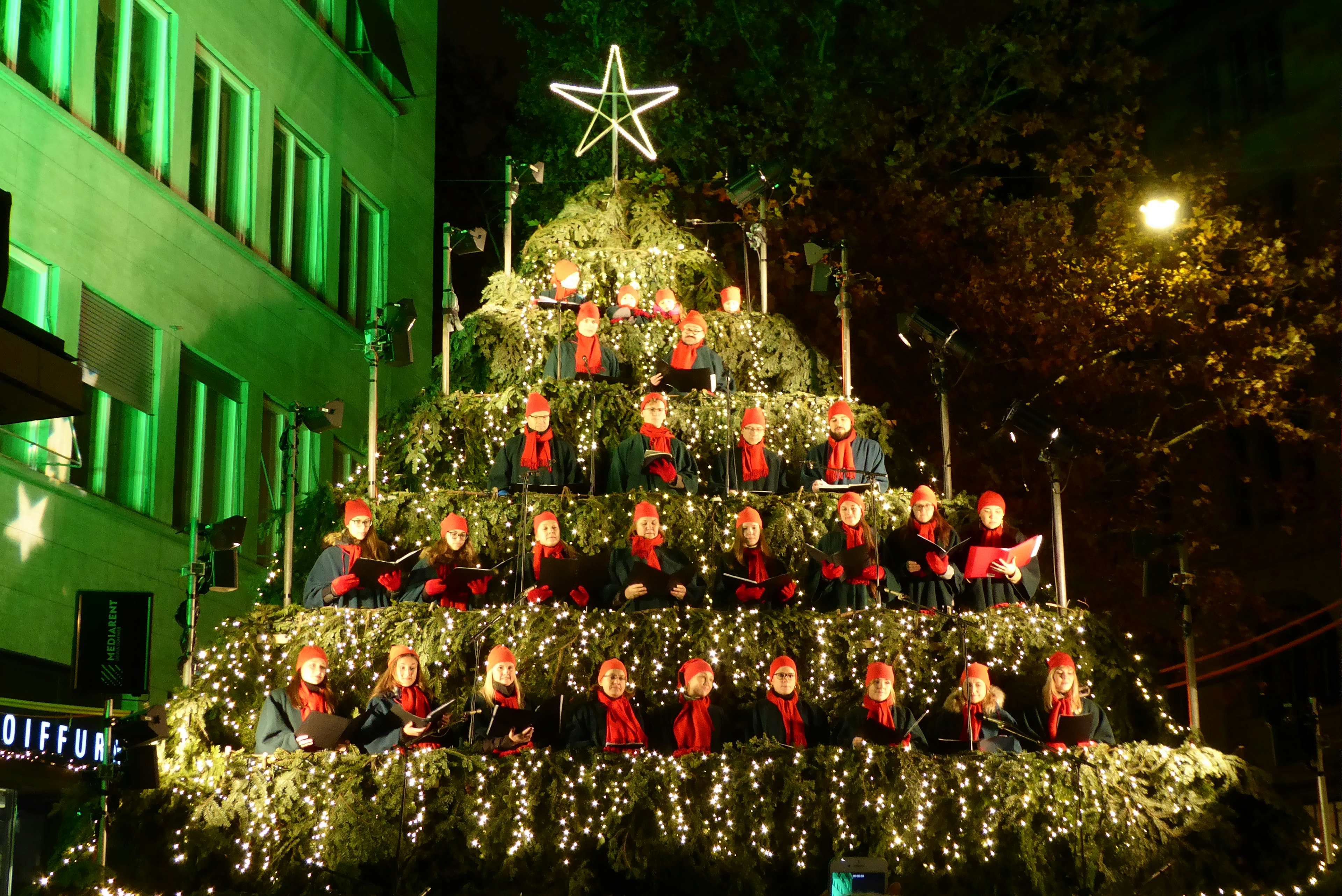 A large Christmas tree with singers dressed in red tucked between the branches