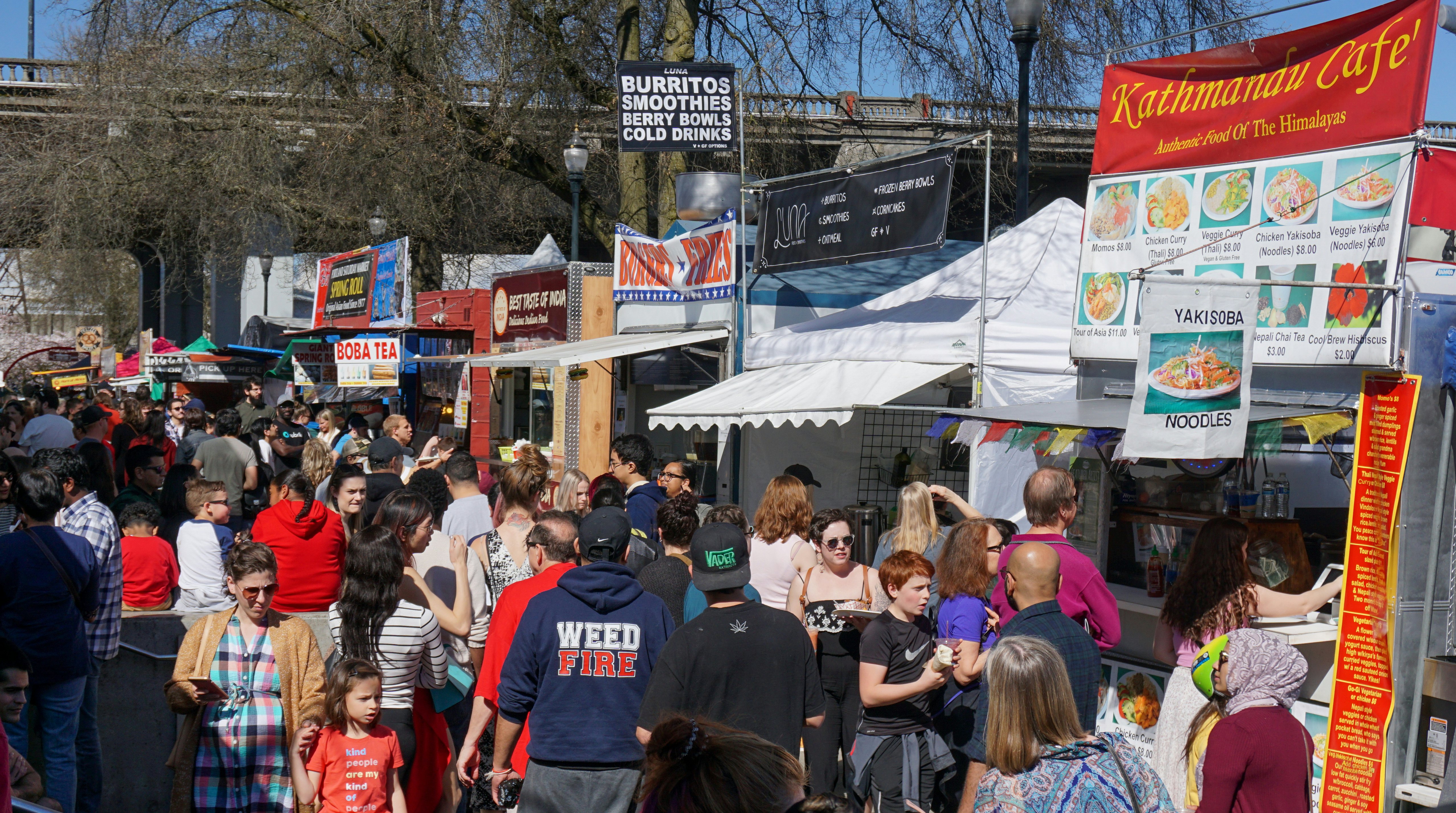 A crowd of people at food carts and booths on a sunny day at at the famous Saturday Market downtown in Waterfront Park, Portland, Oregon, USA