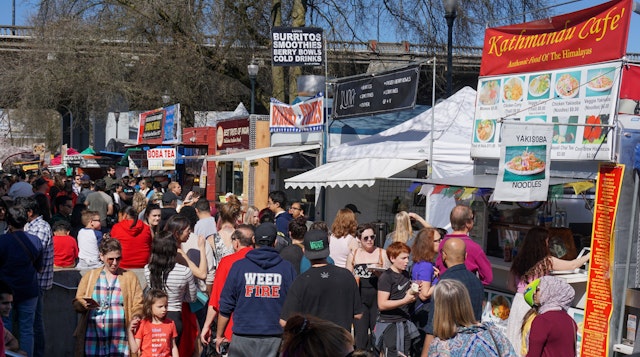A crowd of people at food carts and booths on a sunny day at at the famous Saturday Market downtown in Waterfront Park, Portland, Oregon, USA
