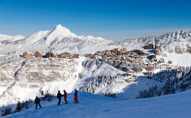 Skiers on a slope. Behind them across the snowy valley a resort is built into the side of a mountain
