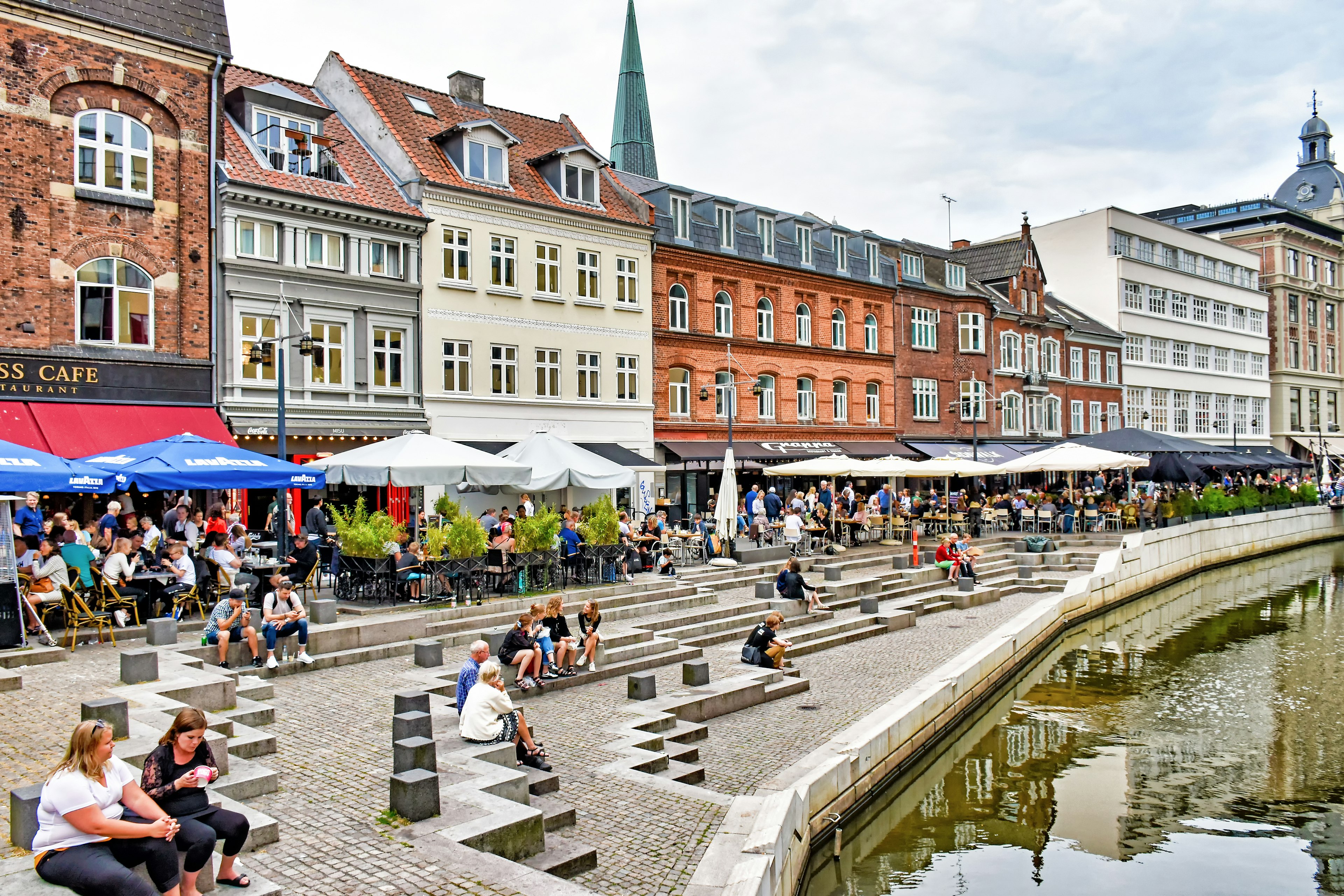 People sit at a harbourside lined with restaurants