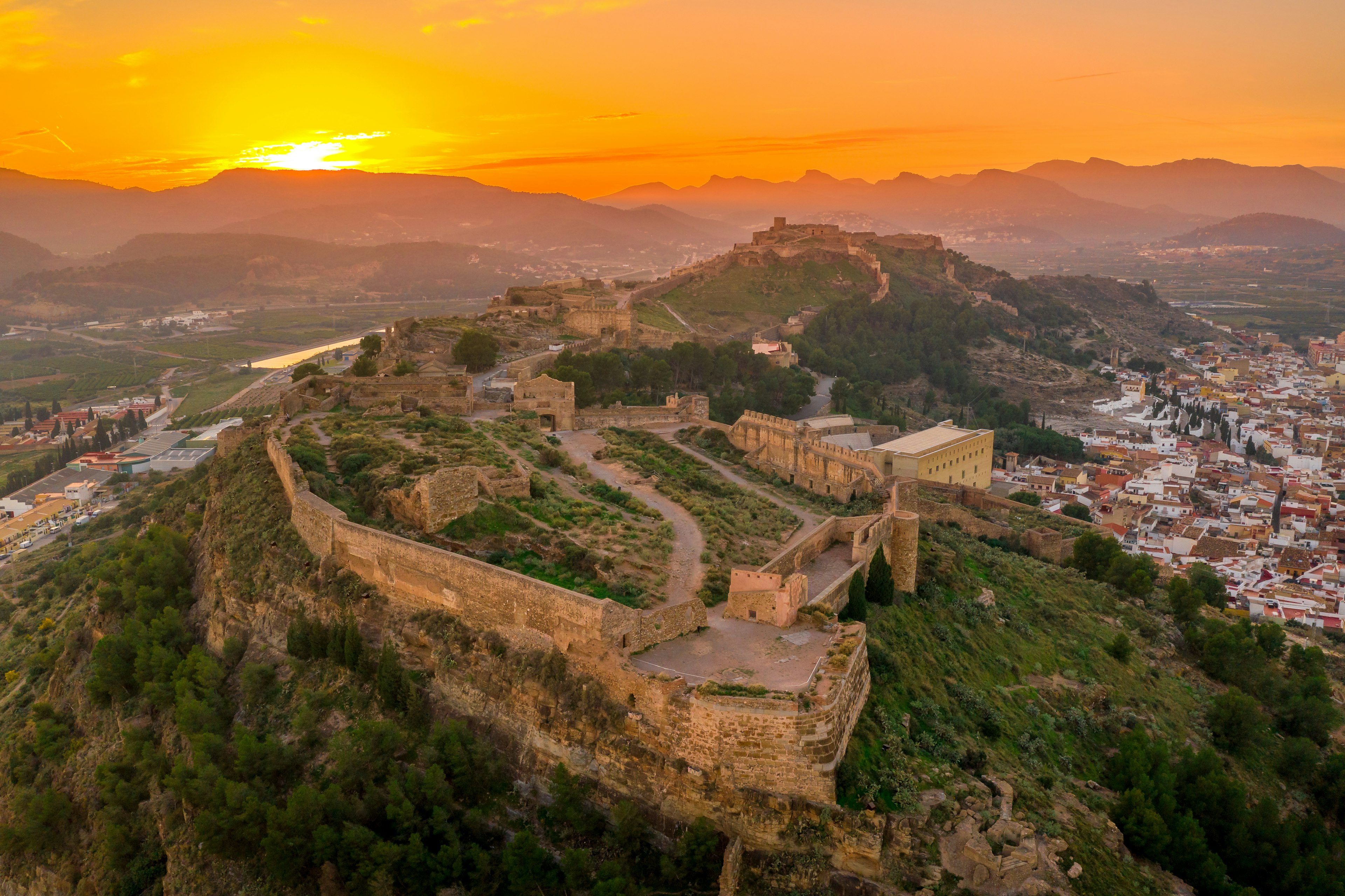 A hilltop fortress with large stone walls at sunset