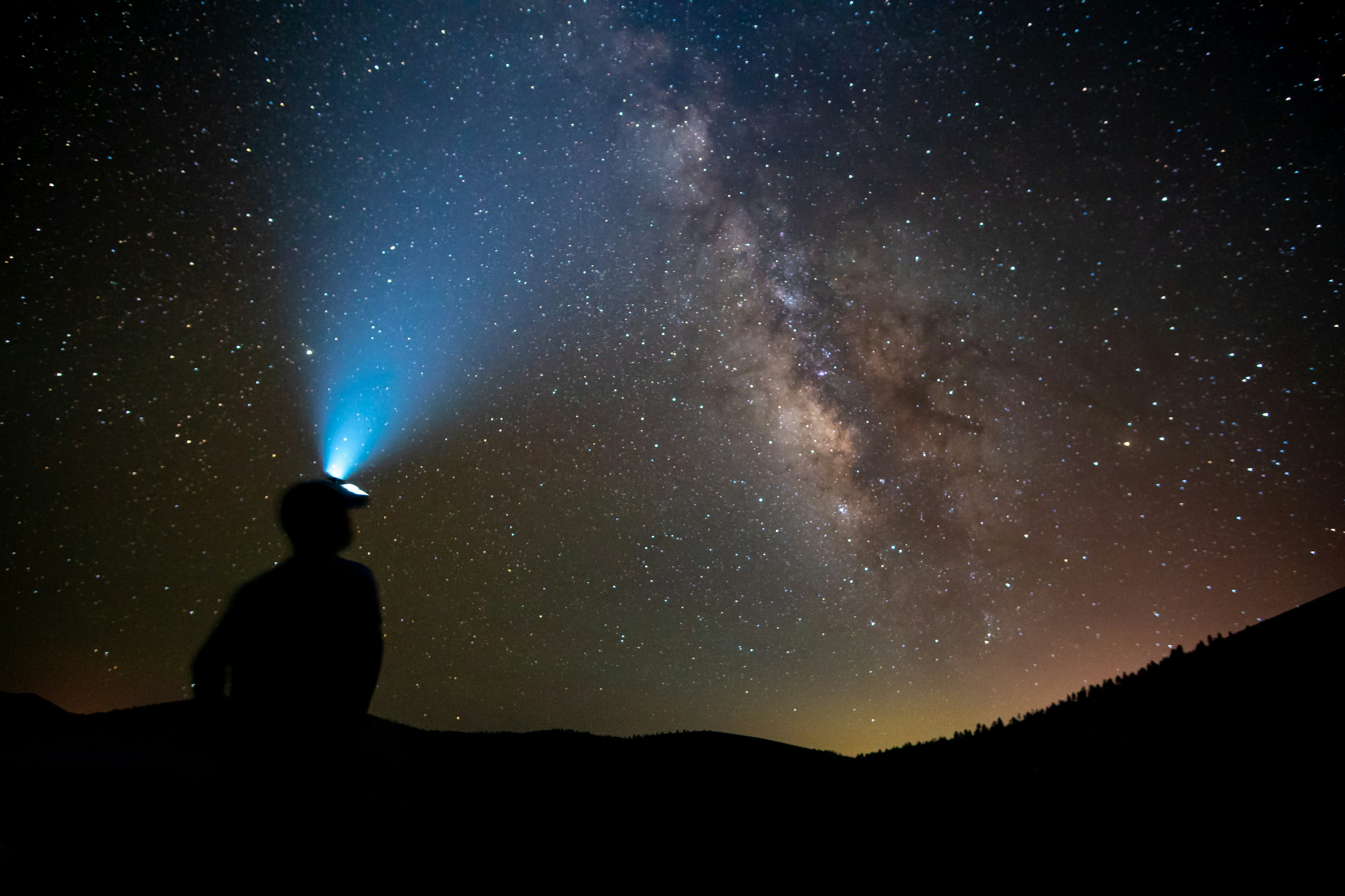 A man with a head lamp looks up toward the millions of starts of the Milky Way at night Flagstaff, Arizona