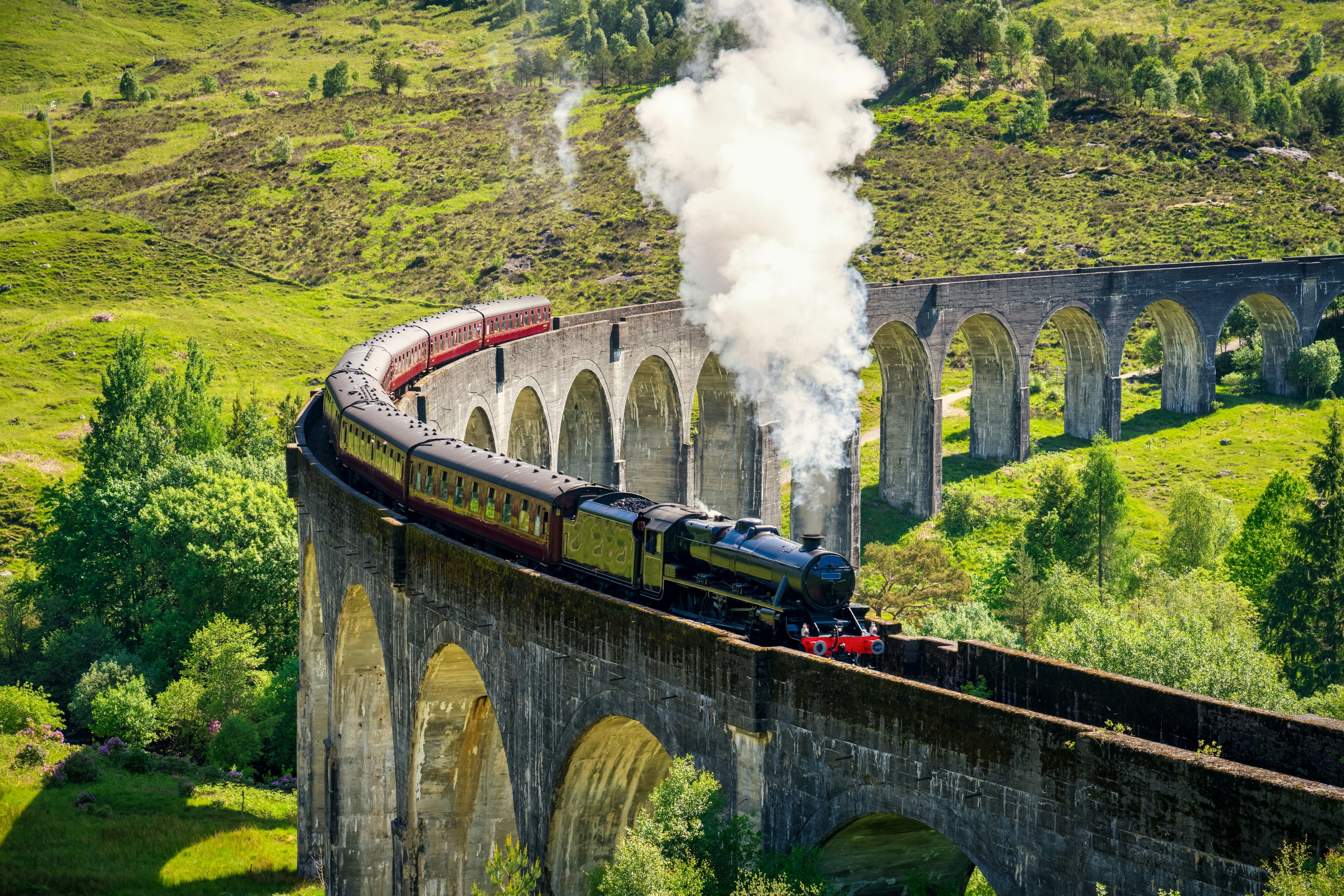 A steam trains rounds a bend on the iconic Glenfinnan Railway Viaduct in Scotland, UK