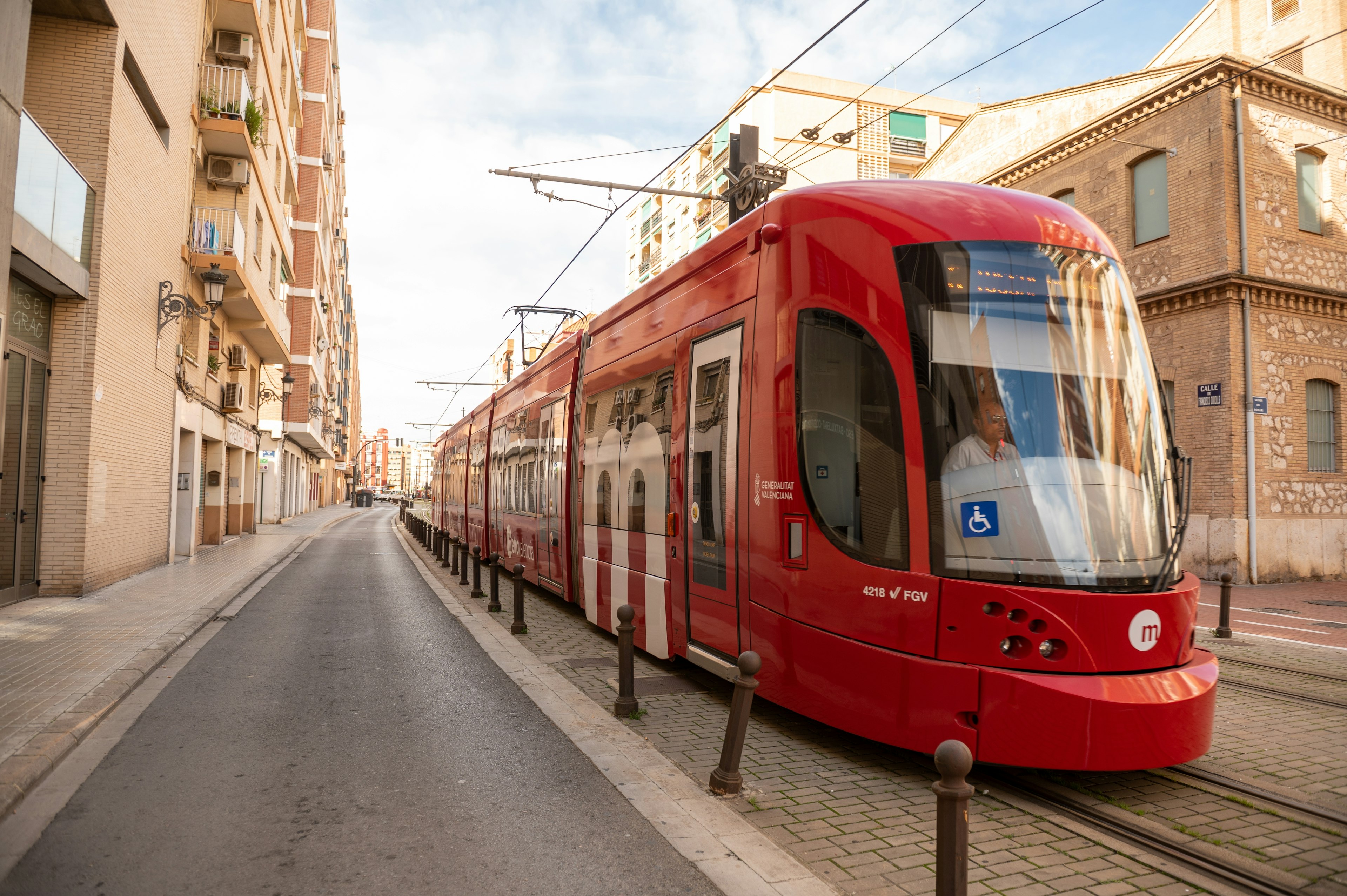 A red tram moves past tan-colored buildings on a city street in Valencia, Spain