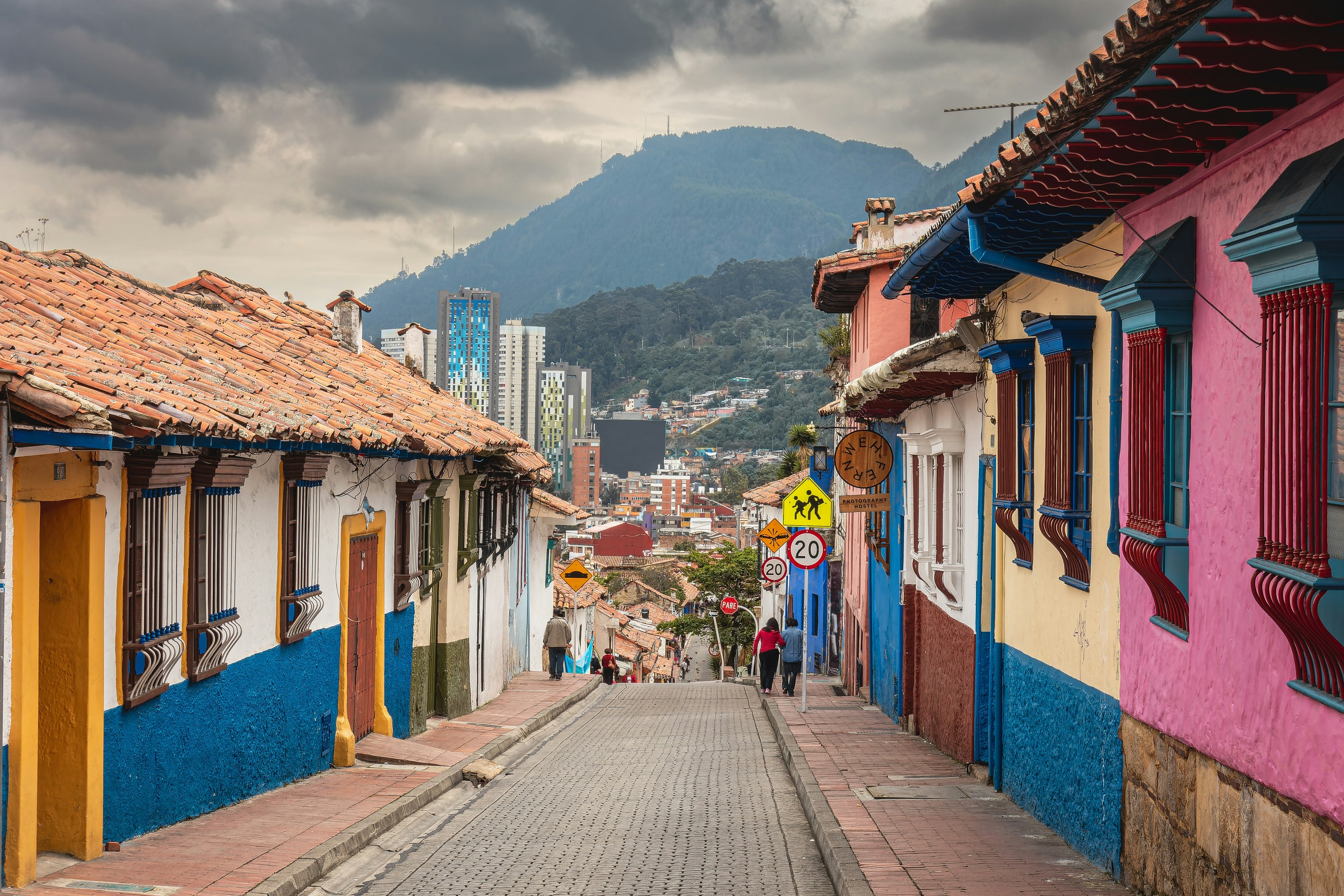 A narrow, cobbled street lined with one-story, brightly painted houses with cloudy mountains in the distance, La Candelaria, ǲǳá, Colombia