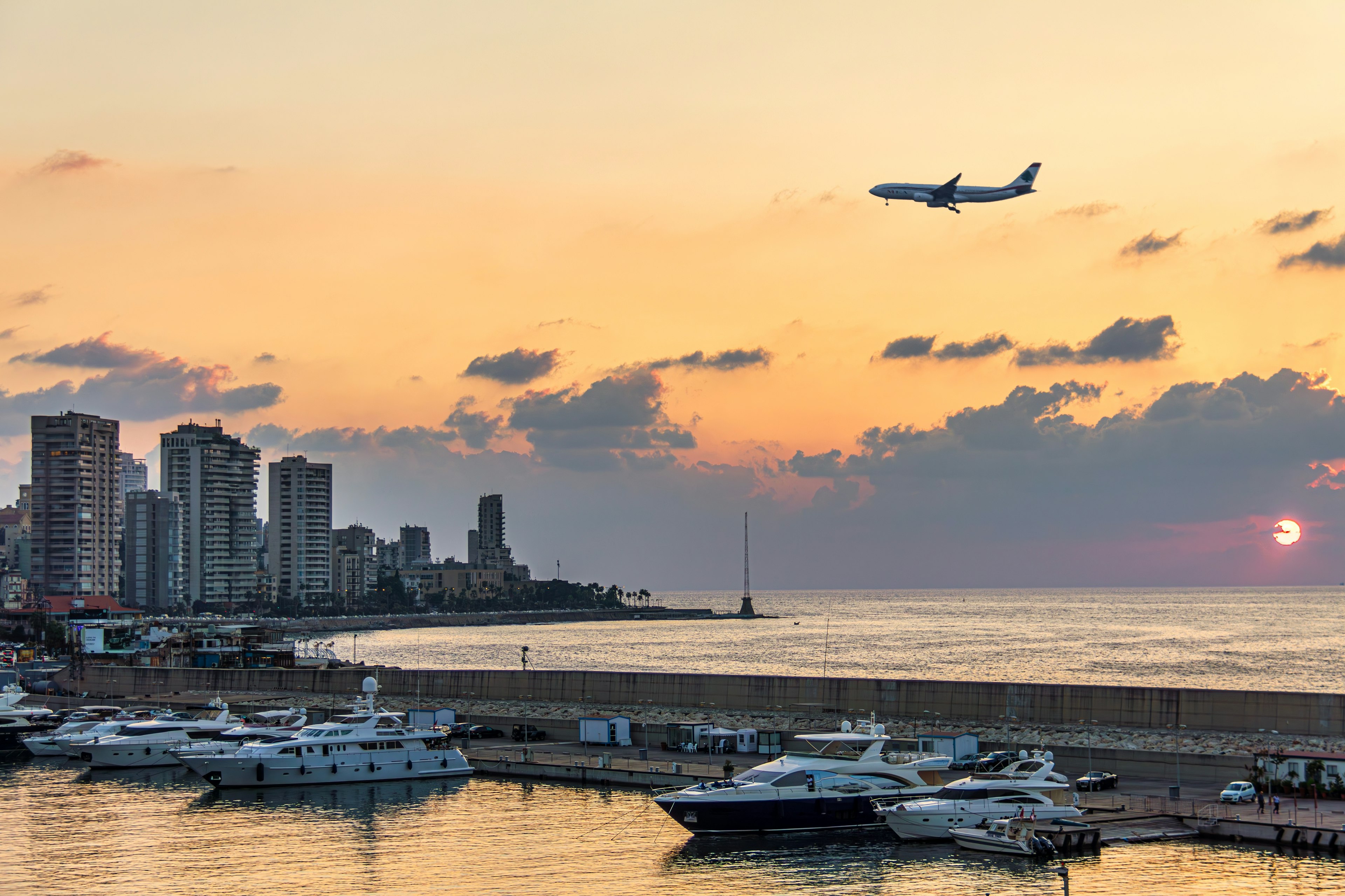 A plane landing over Beirut waterfront skyline during sunset