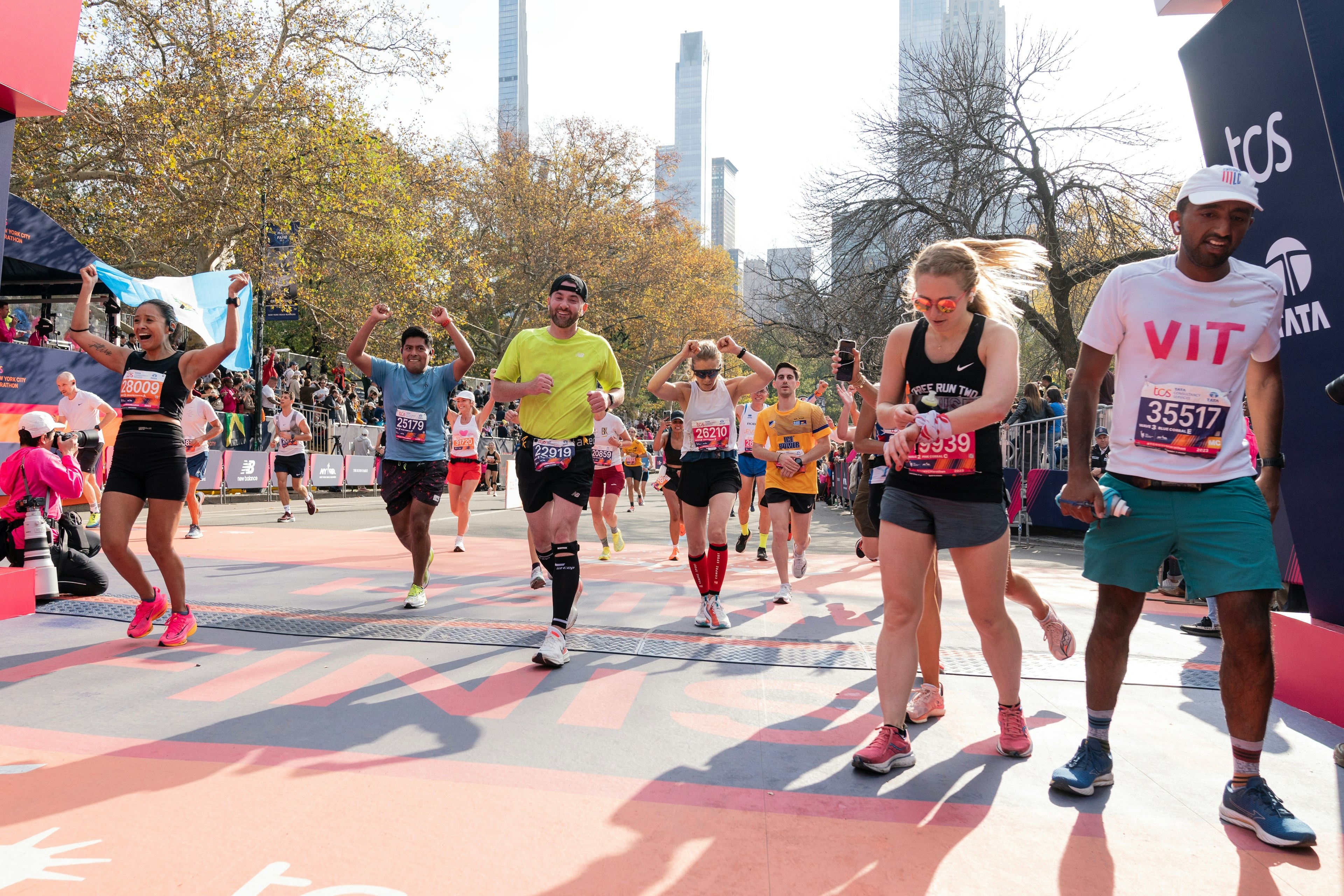 Tired runners cross the finish line of a long-distance race in a city with high-rise buildings