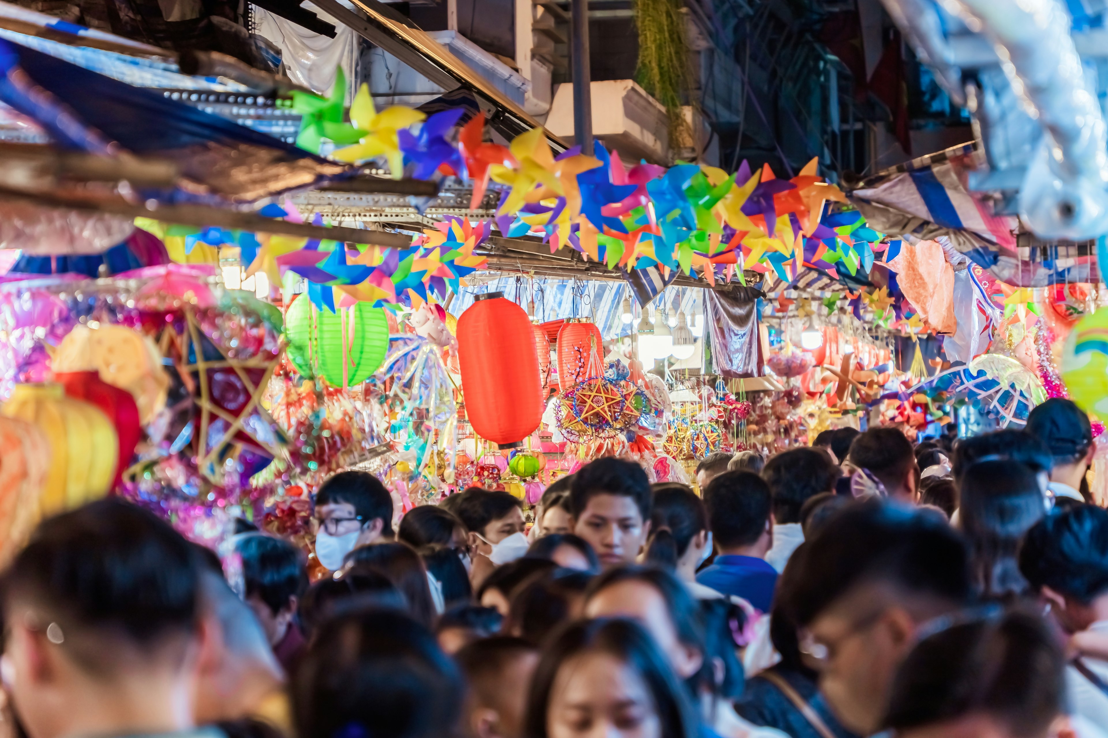 A very busy street with many shoppers. Stalls display colourful lanterns for sale.