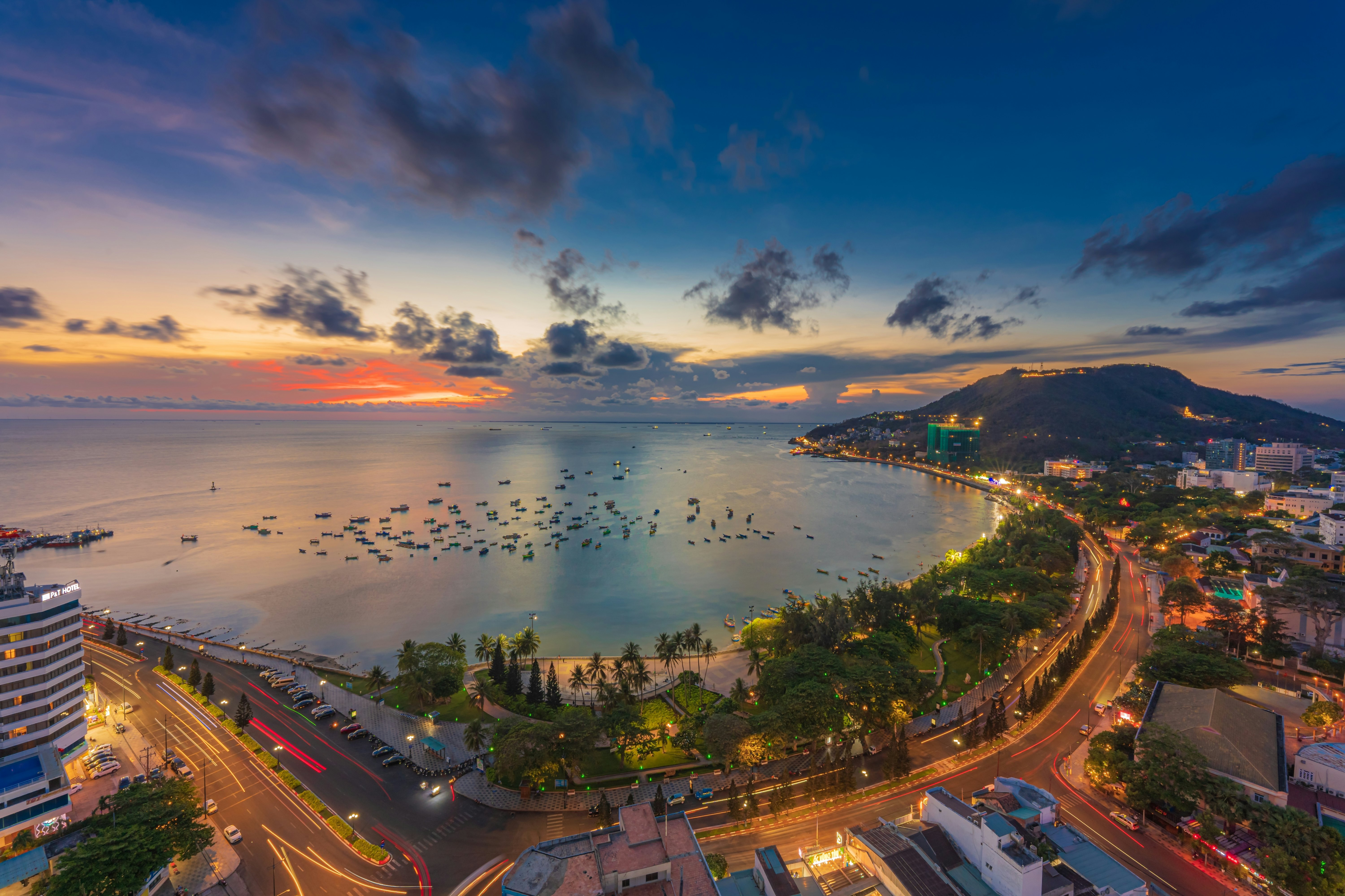 Top view with beautiful sunset and boats. Panoramic view of Vung Tau coast from above with waves, beach, streets, coconut trees and Tao Phung mountain in Vietnam