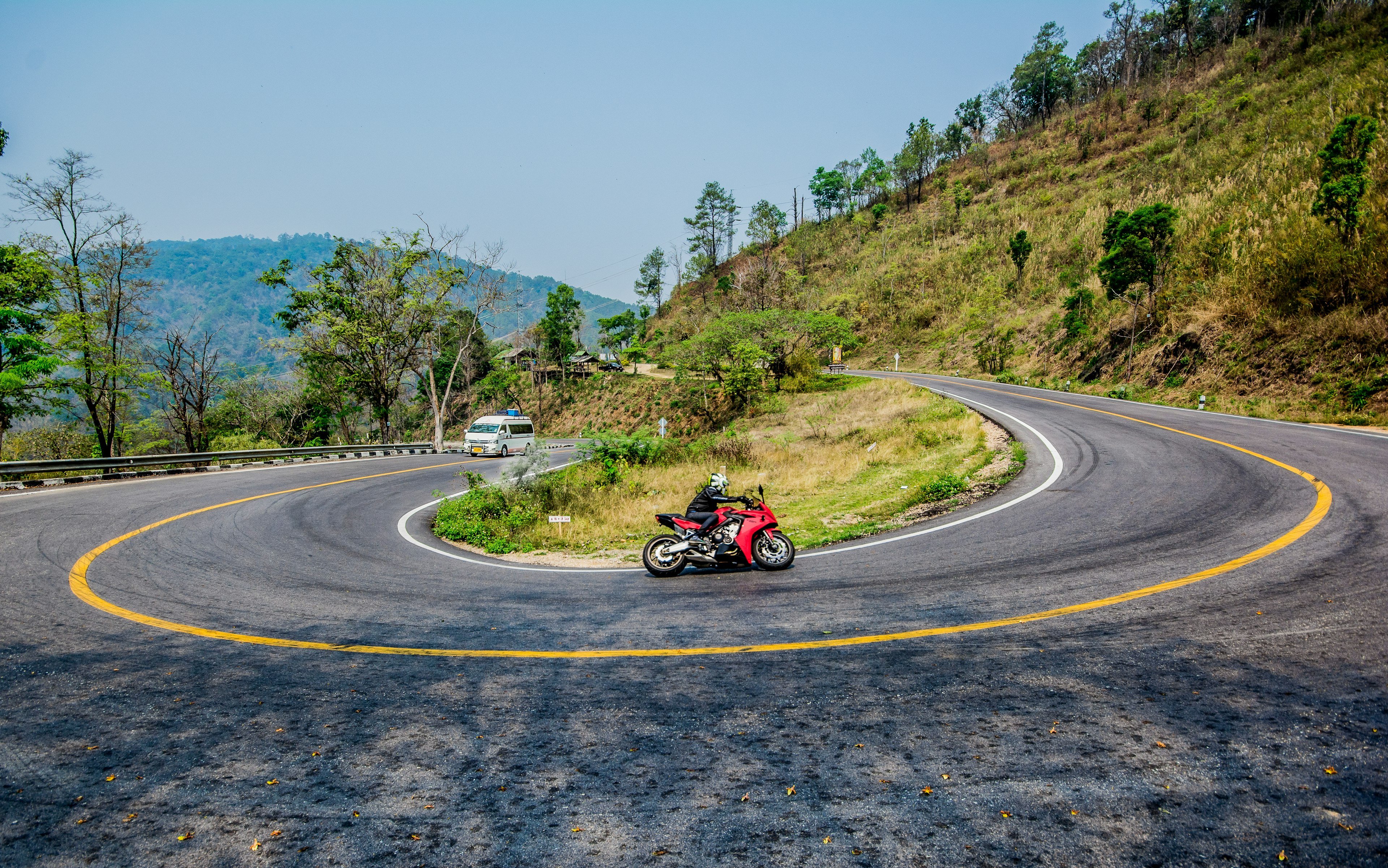 A motorcycle drives around a sharply curved switchback along the Mae Hong Son Loop, which has 1864 curves
