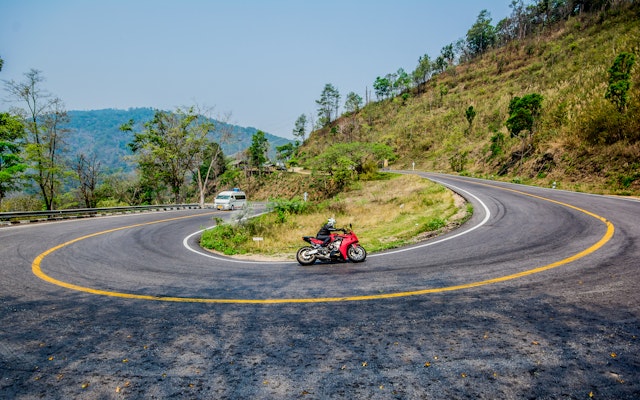 A motorcycle drives around a sharply curved switchback along the Mae Hong Son Loop, which has 1864 curves