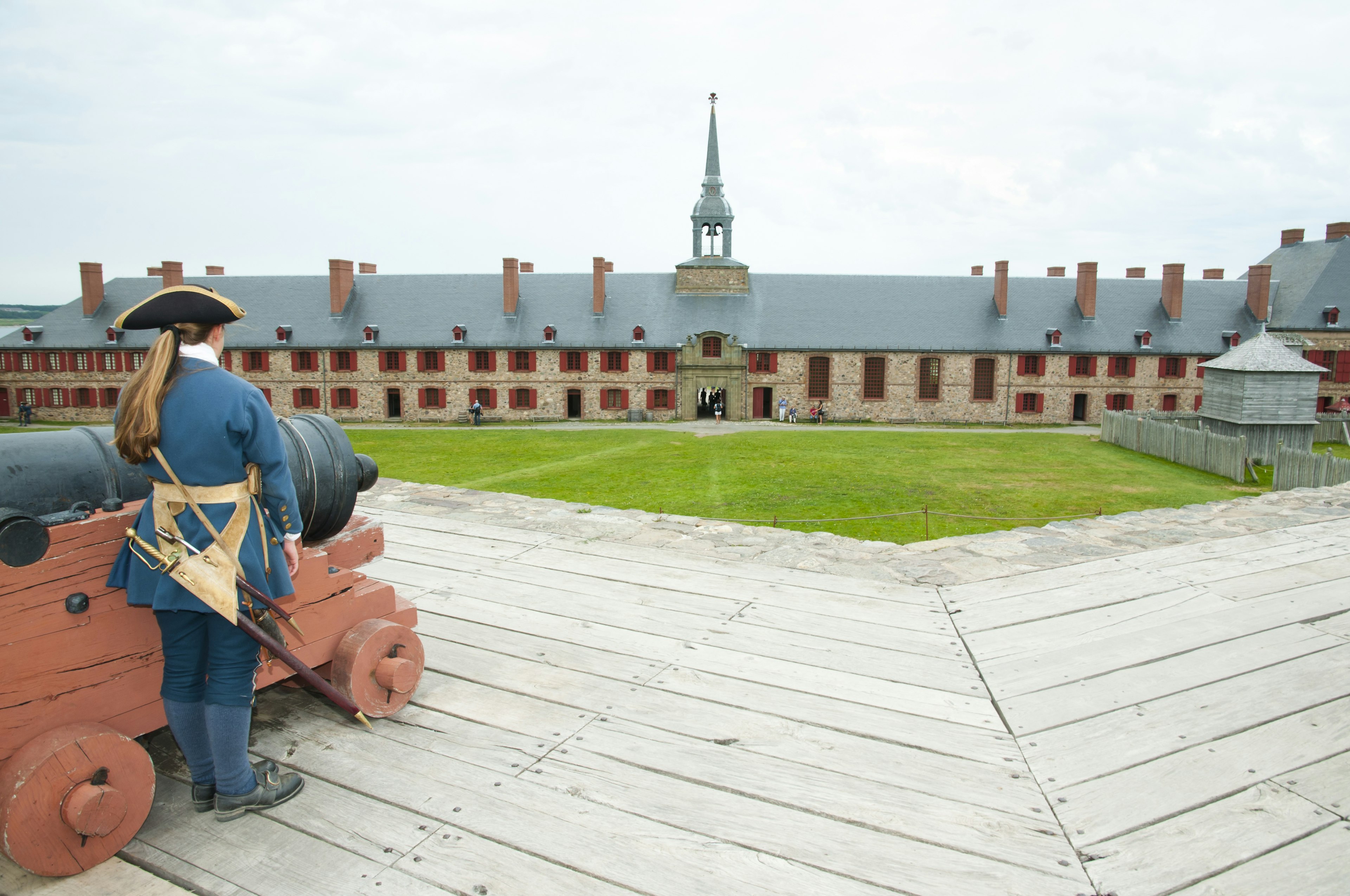 A costumed guide stands near a cannon in front of a fortress