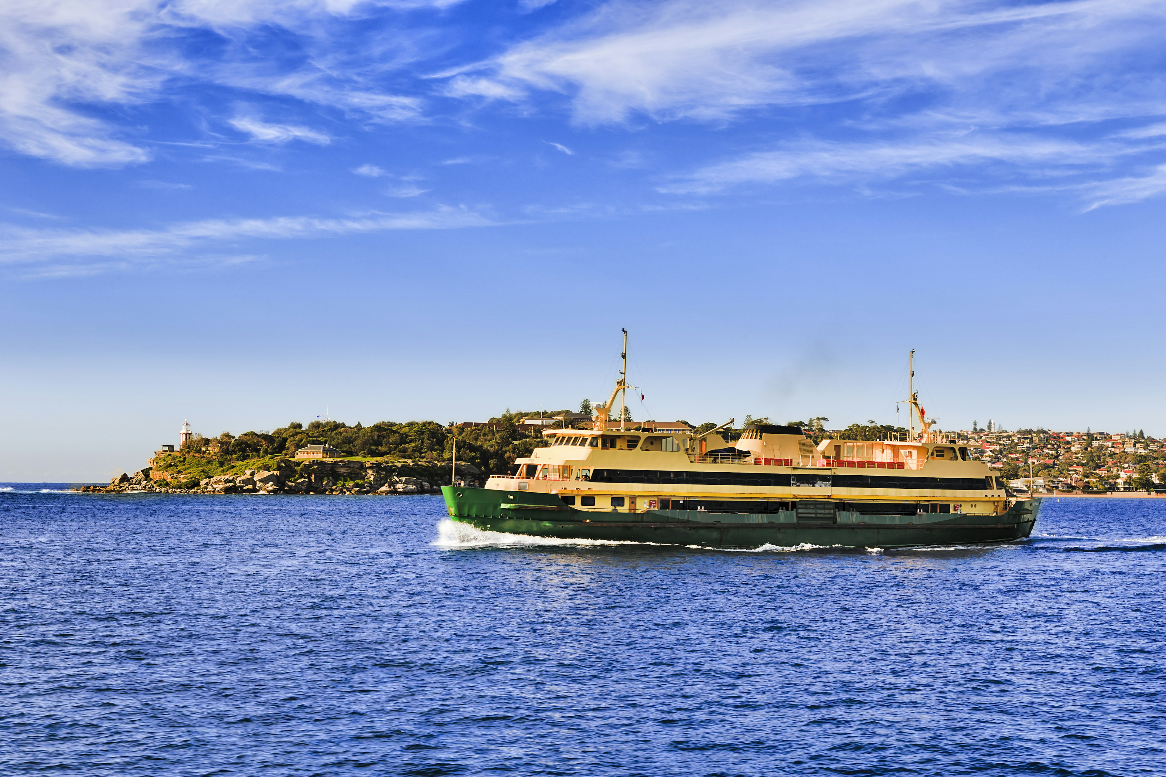 Passenger ferry in the middle of Sydney harbour en route to Manly from city wharf transporting commuters on a sunny day in view of South Head lighthouse.