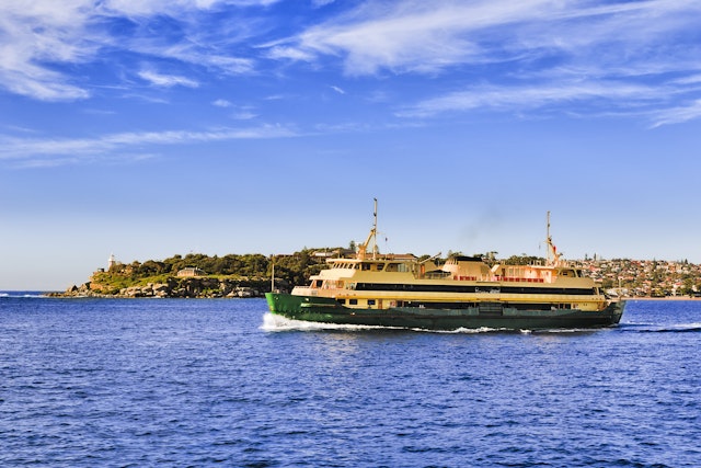 Passenger ferry in the middle of Sydney harbour en route to Manly from city wharf transporting commuters on a sunny day in view of South Head lighthouse.