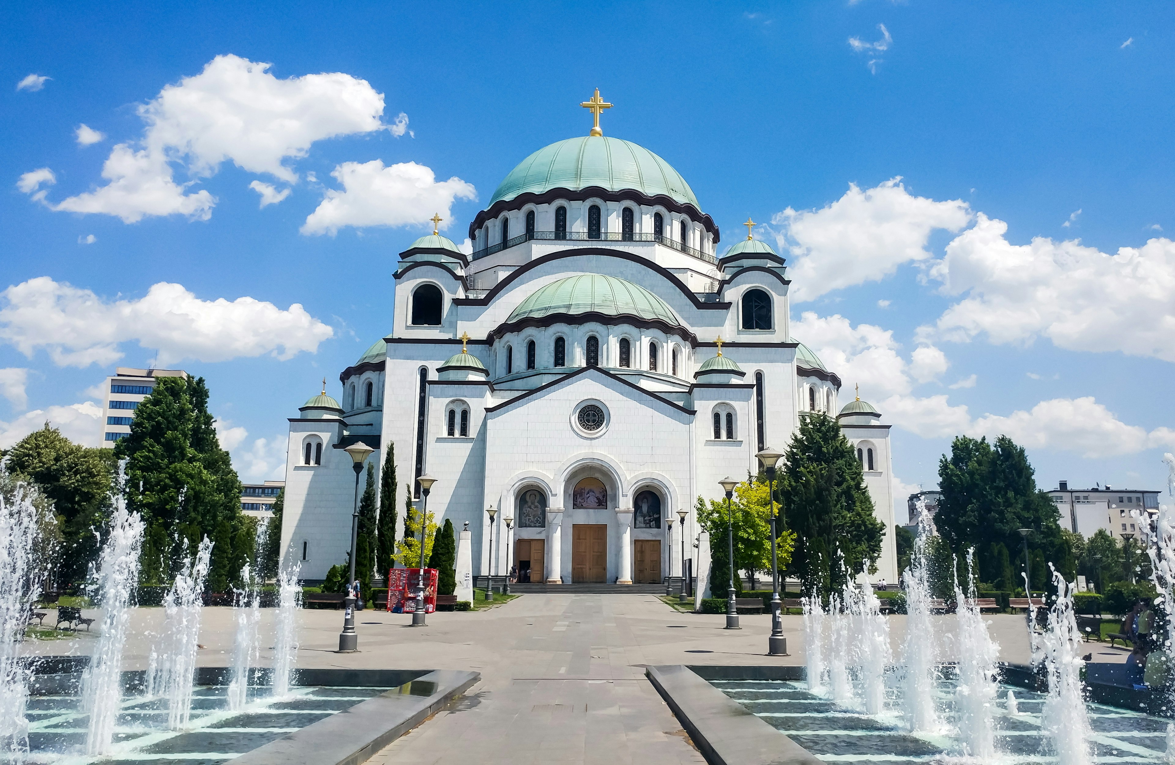 A huge white church with a green dome. Fountains are bubbling on the path approaching the main door