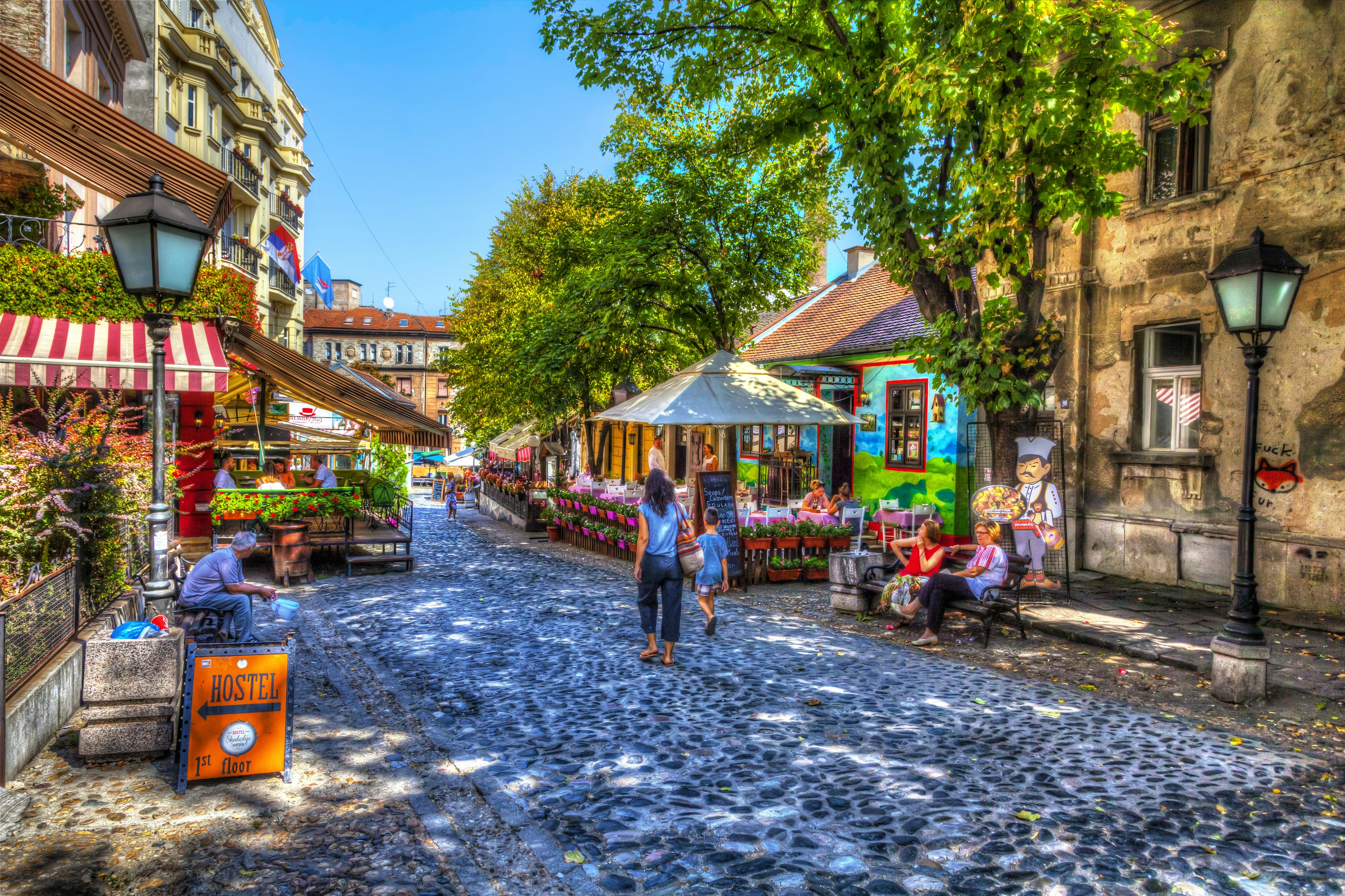 A mother and son wander down a cobbled street lined with restaurants and shops with colorful facades