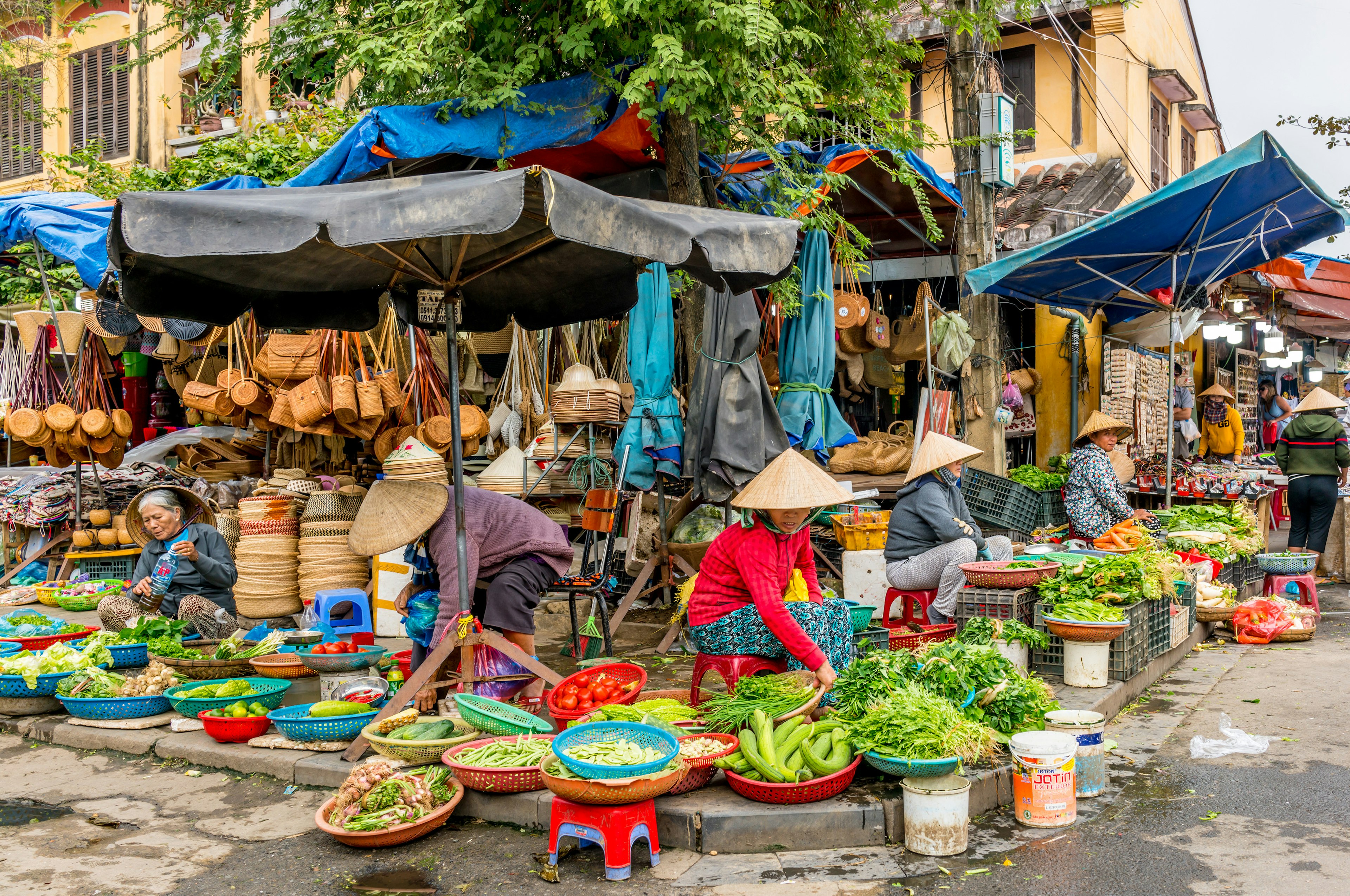 Several traders have set up stalls underneath blue umbrellas, selling fruit, conical hats, baskets and bags.